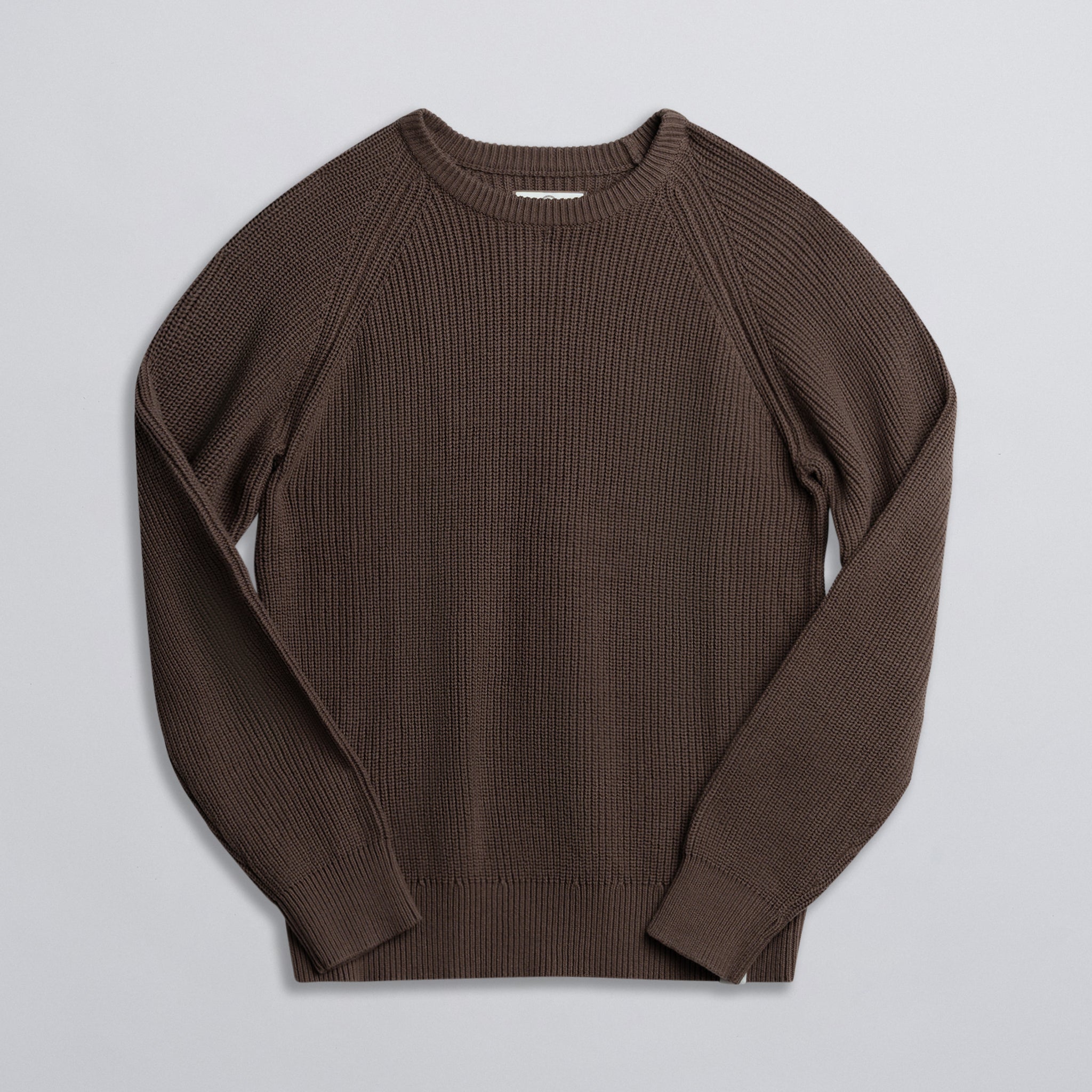 A brown fisherman sweater laid flat on a plain surface.