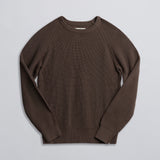 A brown fisherman sweater laid flat on a plain surface.