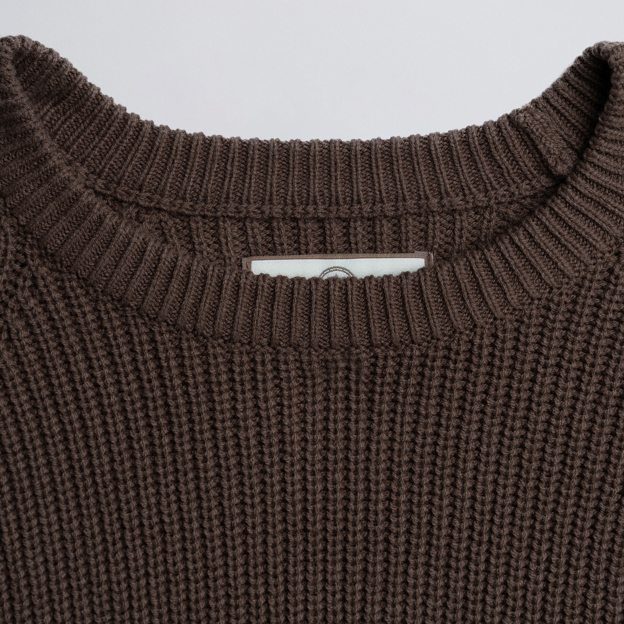 Close-up of a brown knitted sweater collar on a plain background.