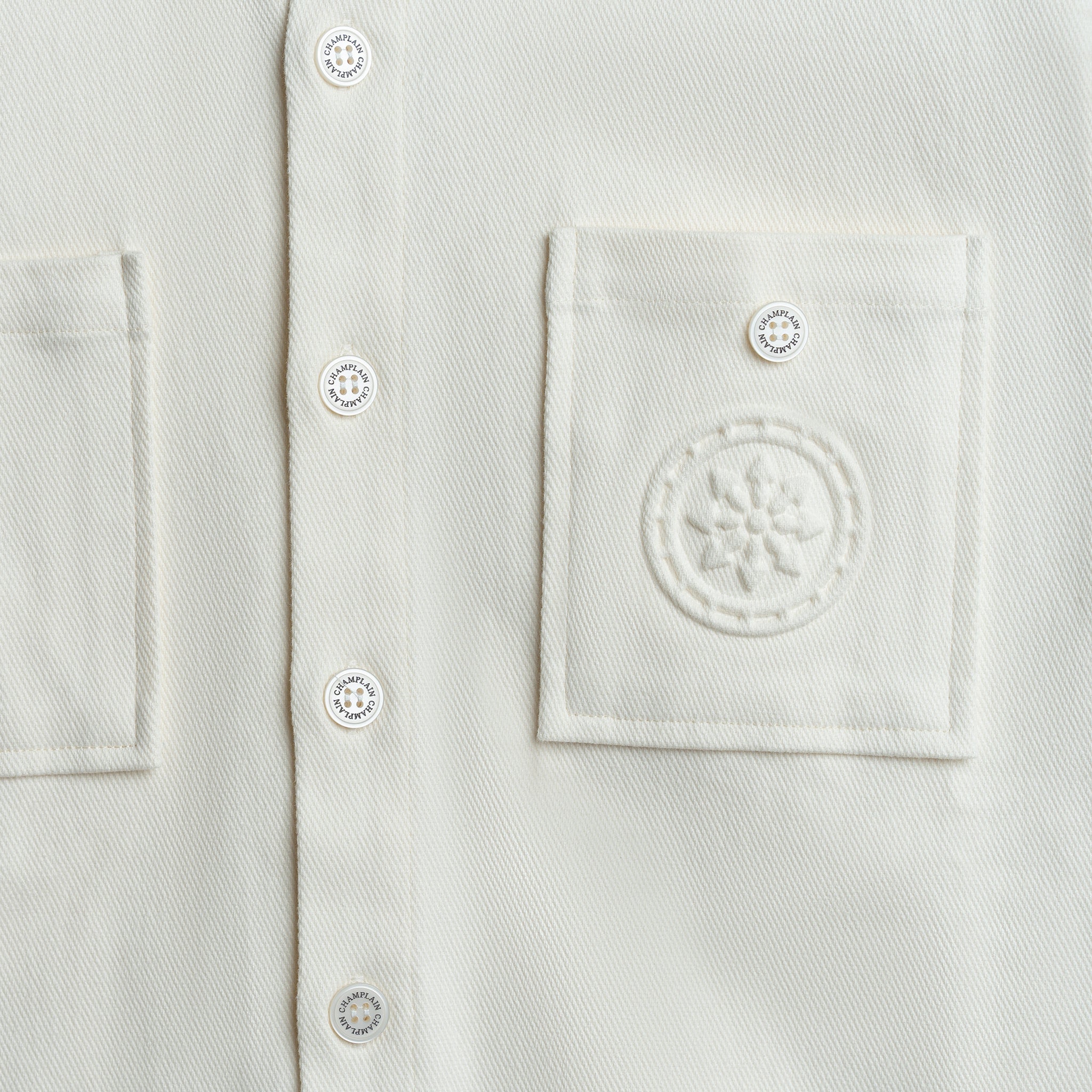 Close-up of a white shirt with button details and a logo on the chest pocket.
