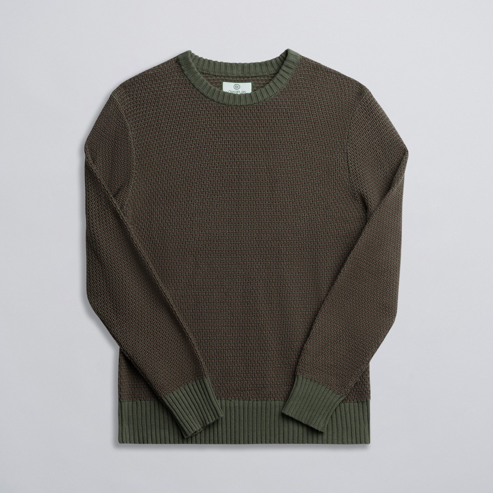 A green and brown two-tone knit sweater displayed against a neutral background