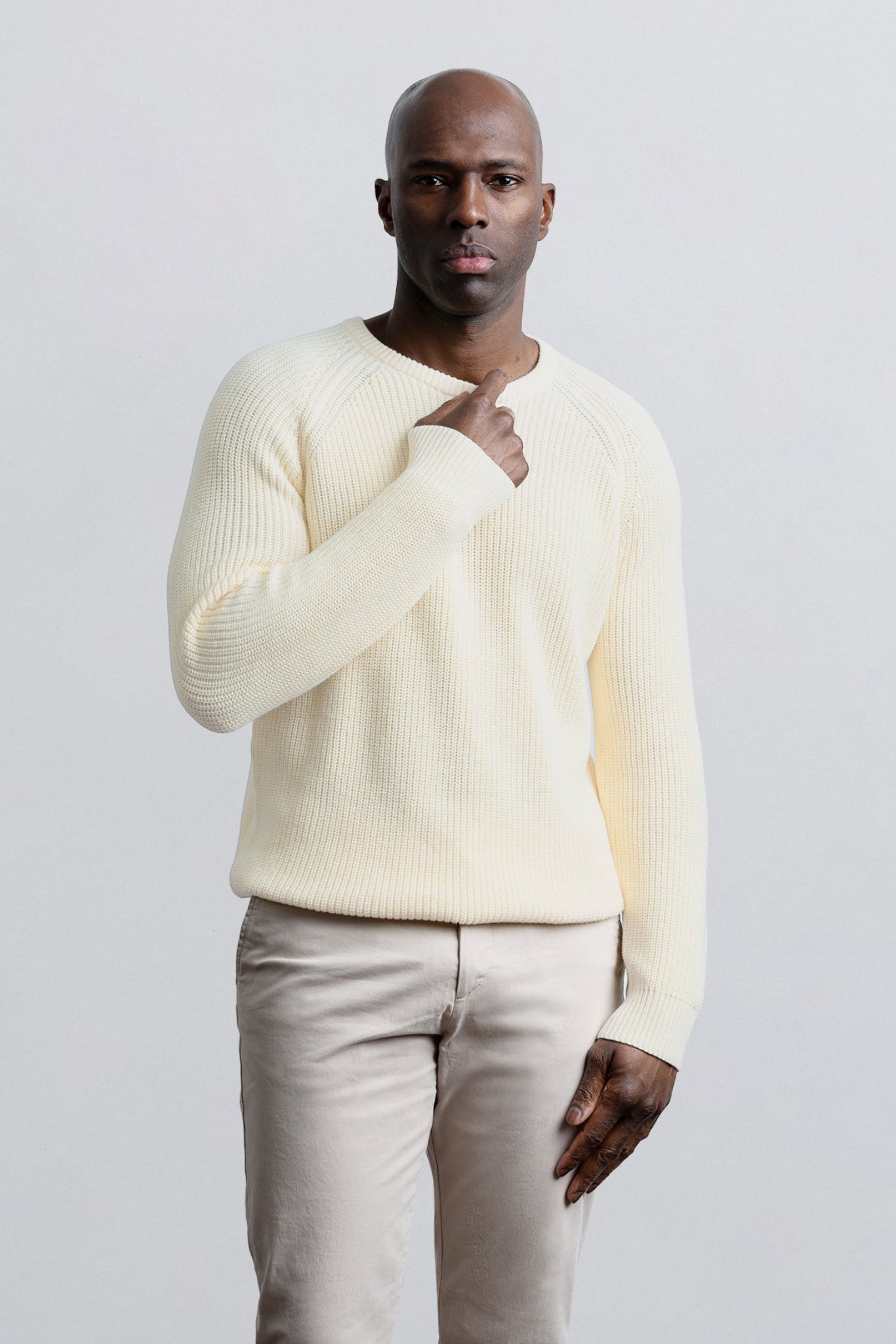 Man wearing a cream sweater and beige pants against a light gray background