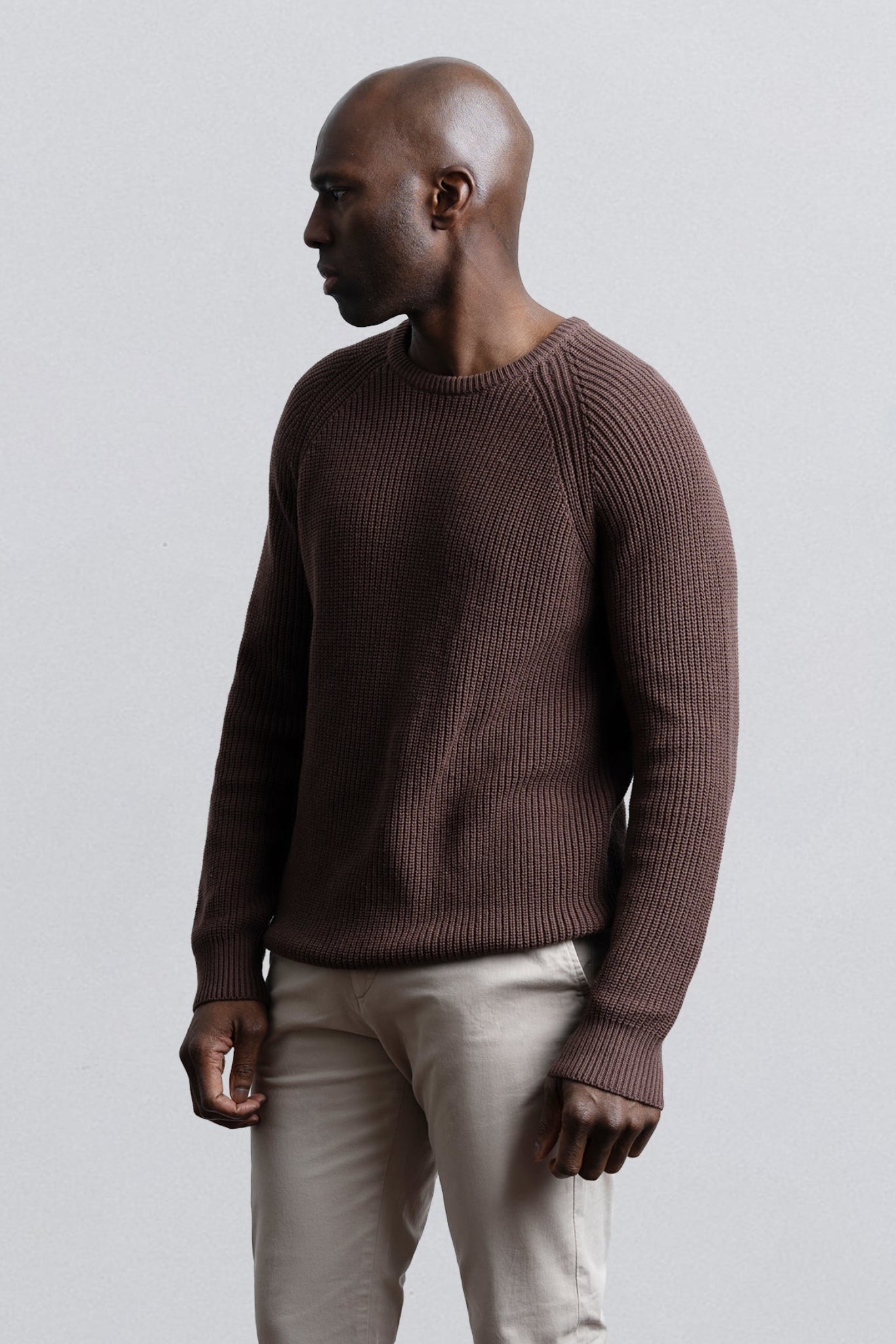 Man wearing a brown sweater and beige pants against a light gray background