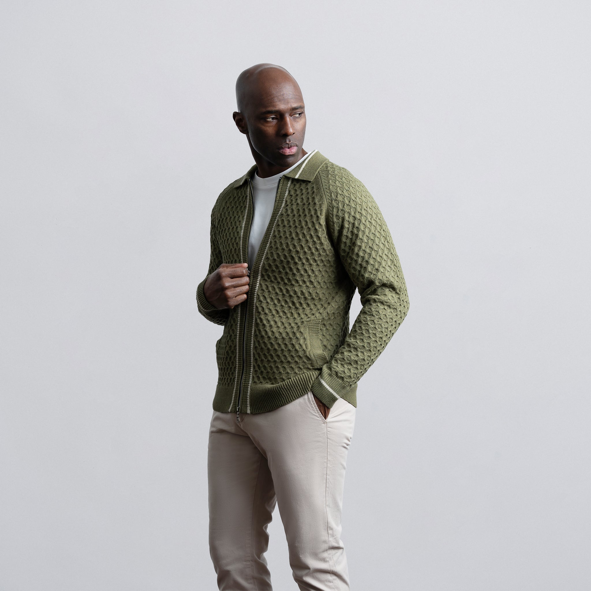 Man wearing a green textured sweater over a white shirt on a light gray background