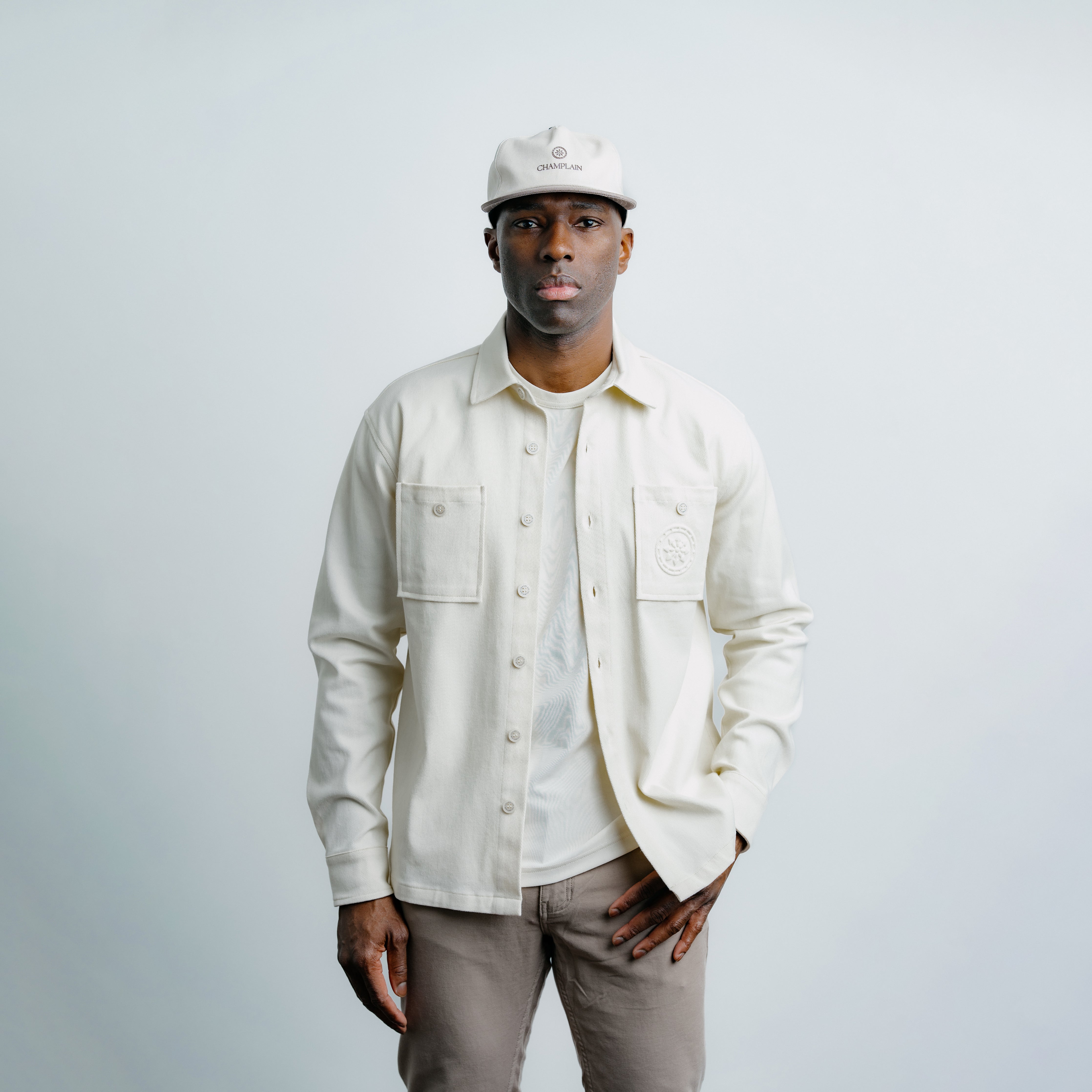 Man wearing a cream champlain overshirt, white t shirt, and beige pants against a light gray background.