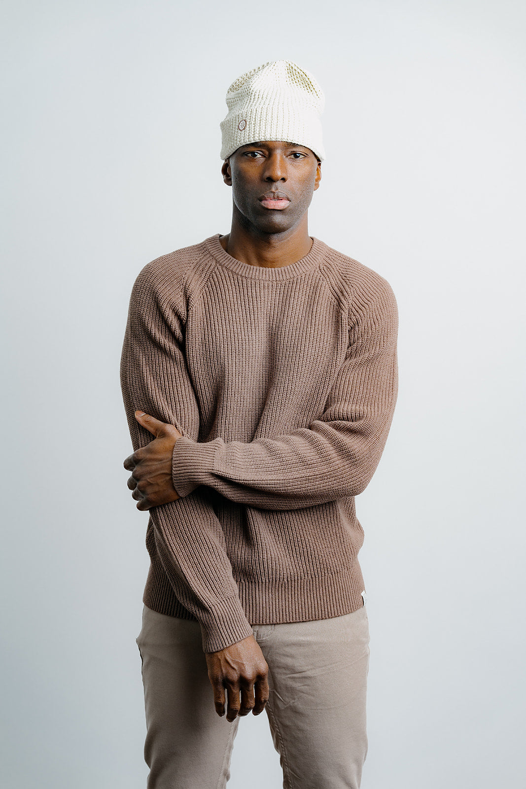 Man wearing a brown sweater and white beanie against a plain background