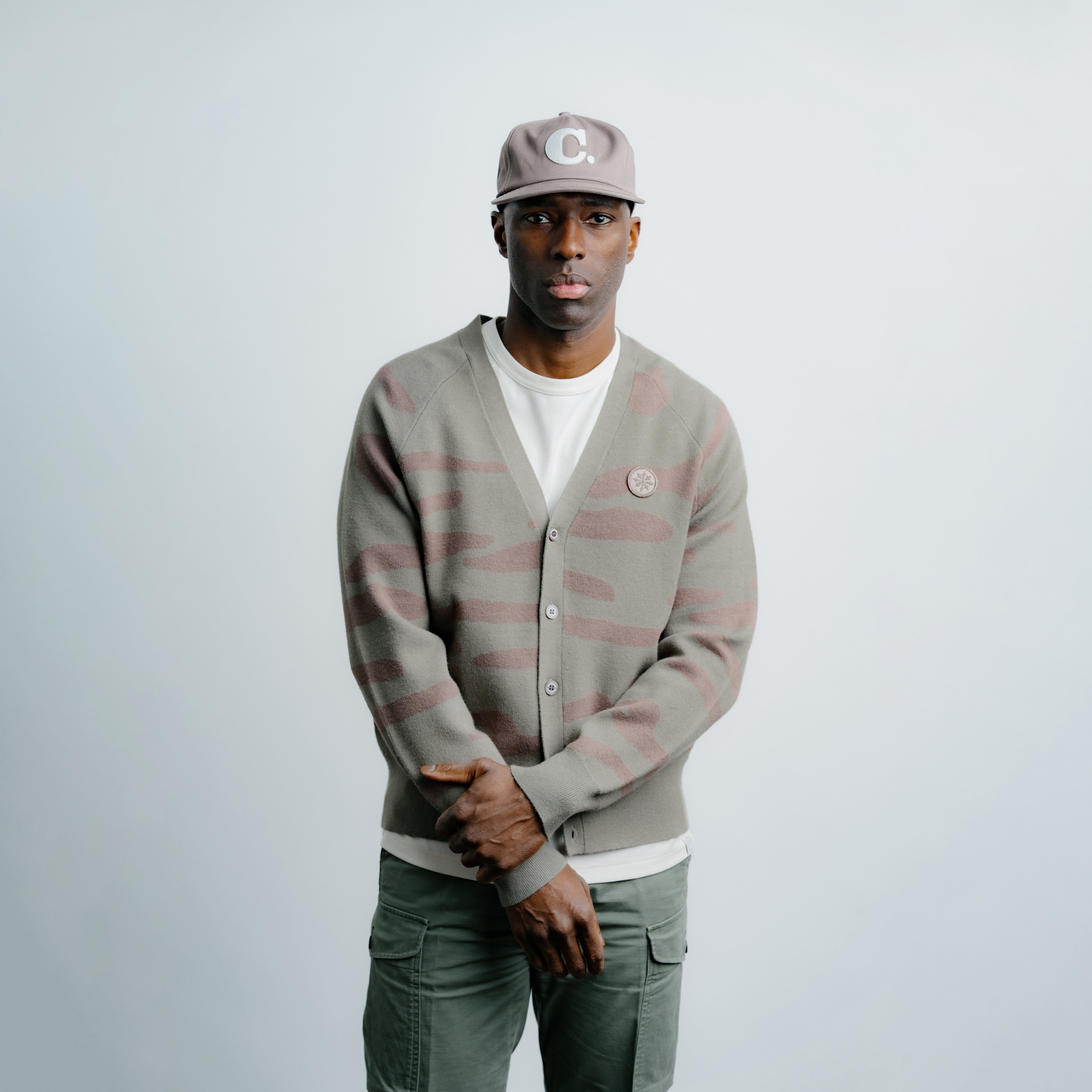 Man wearing a striped cardigan, cap, and pants on a light gray background
