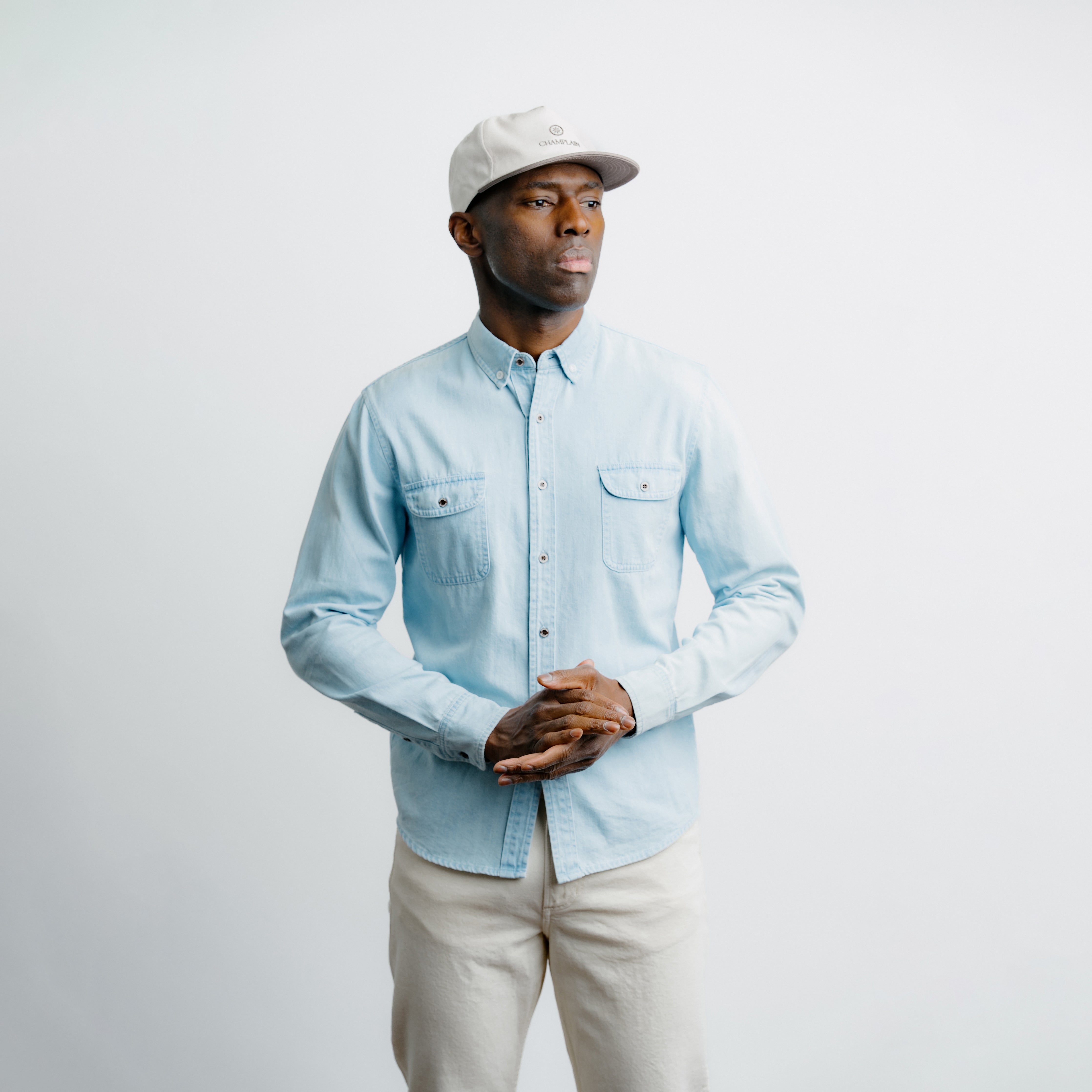 Man wearing a light blue denim shirt and beige cap on a plain background.