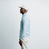Man wearing a light blue shirt and white cap against a plain background