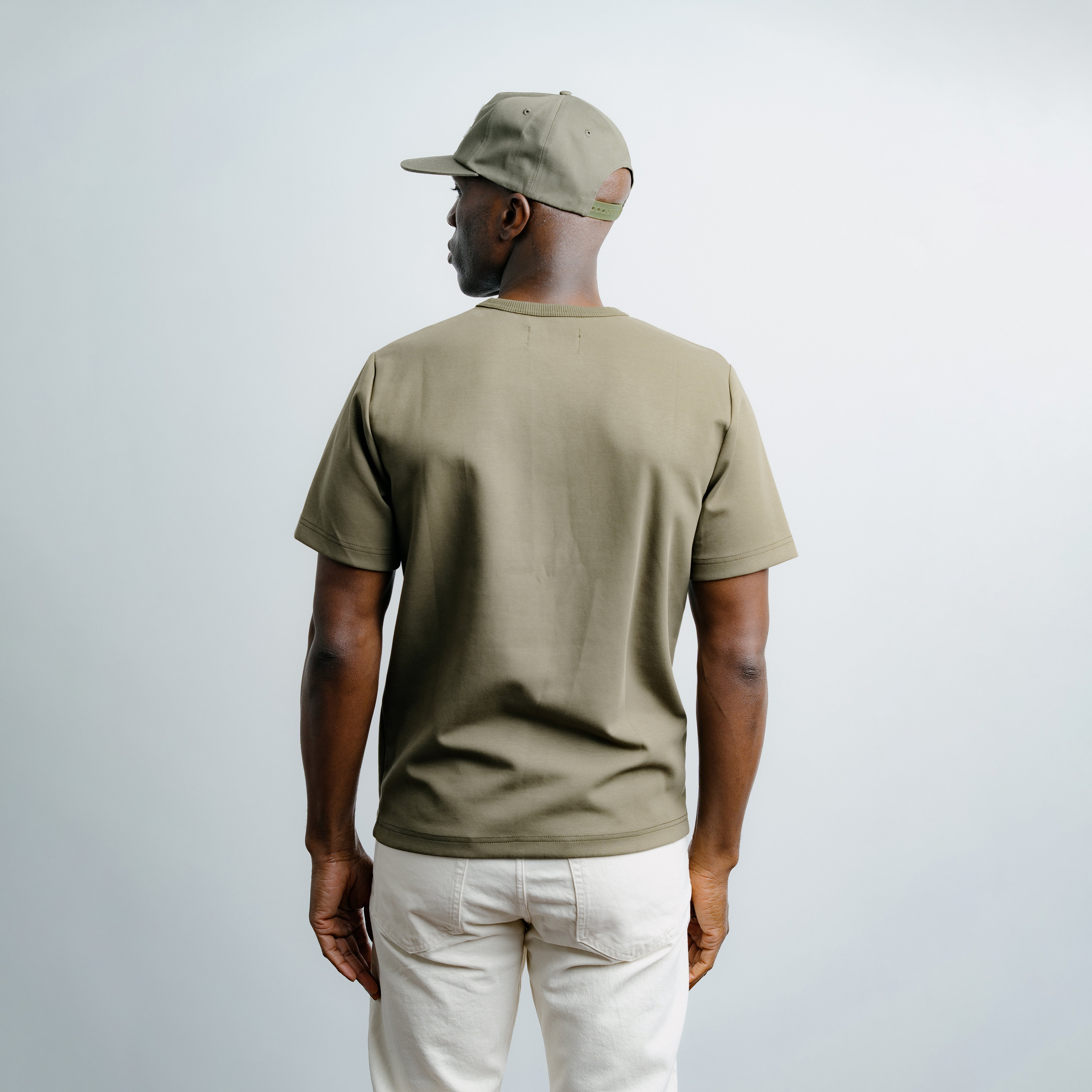 Man wearing a beige cap and olive green t-shirt on a plain background