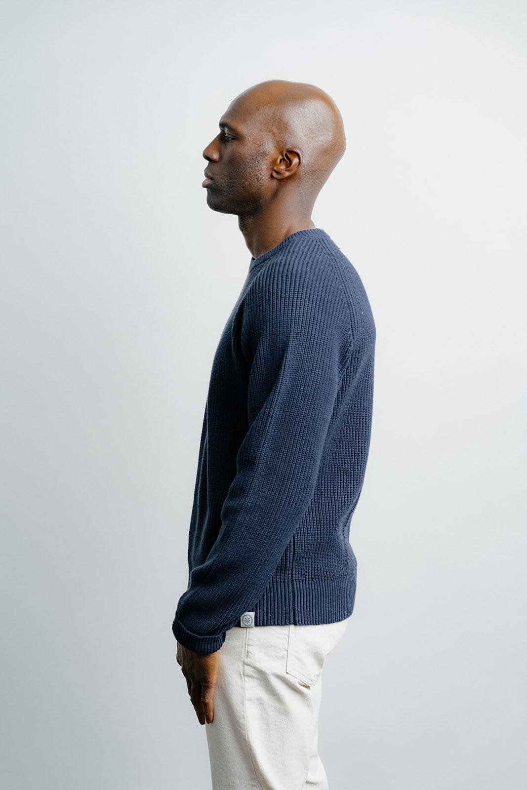 Man wearing a blue sweater and white pants against a plain background