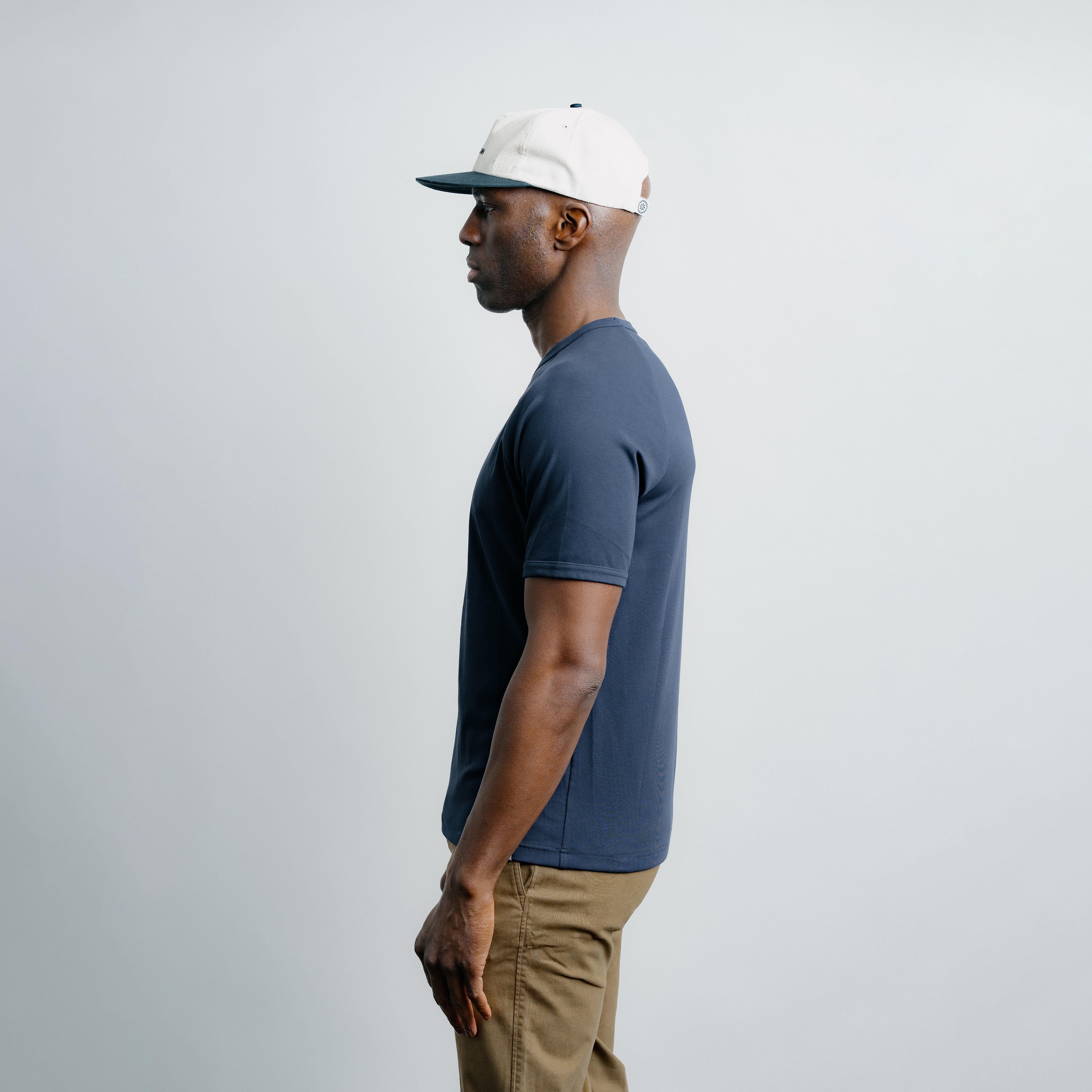 Man wearing a blue t-shirt and beige pants against a plain background