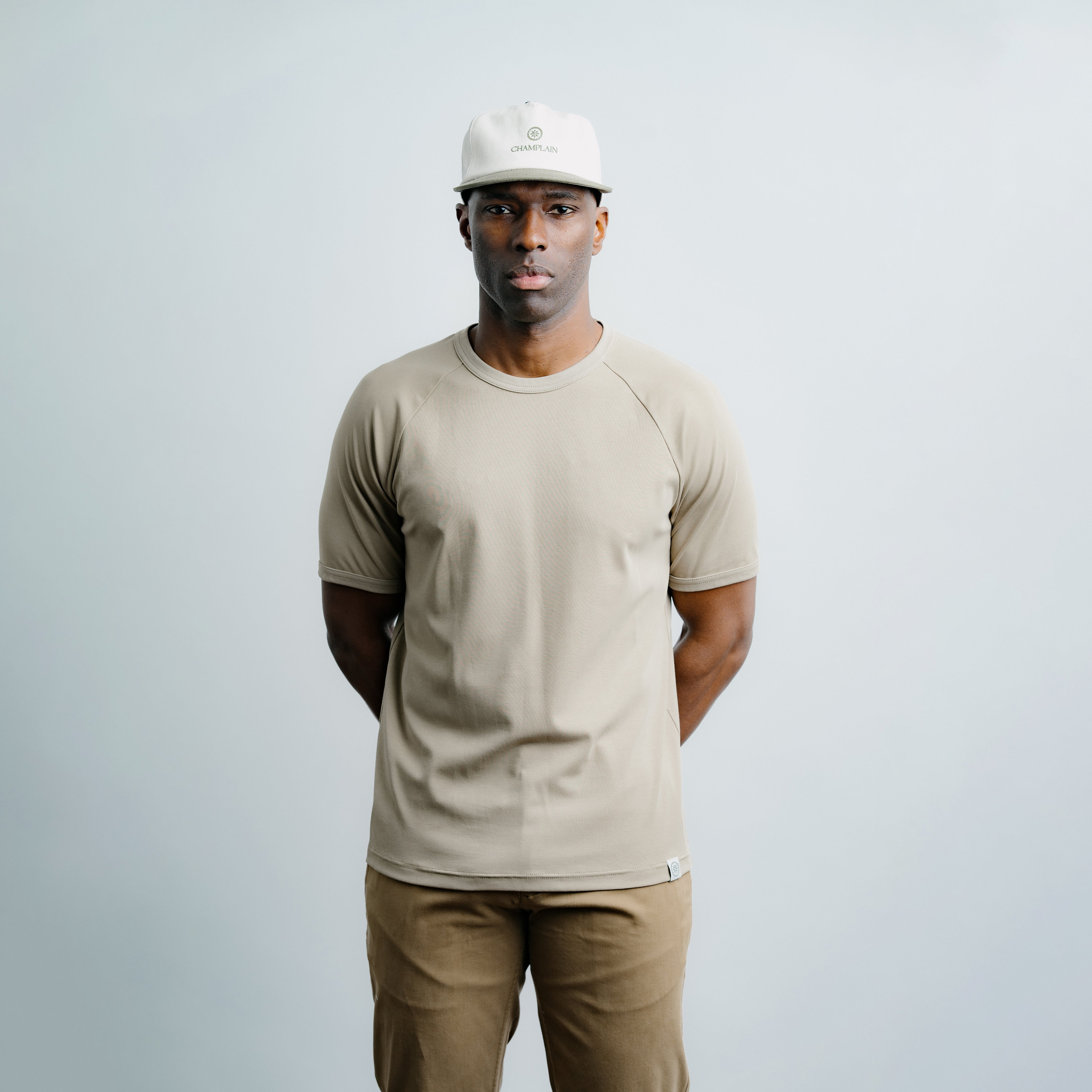 Man wearing a beige t-shirt and pants with a white cap on a light gray background
