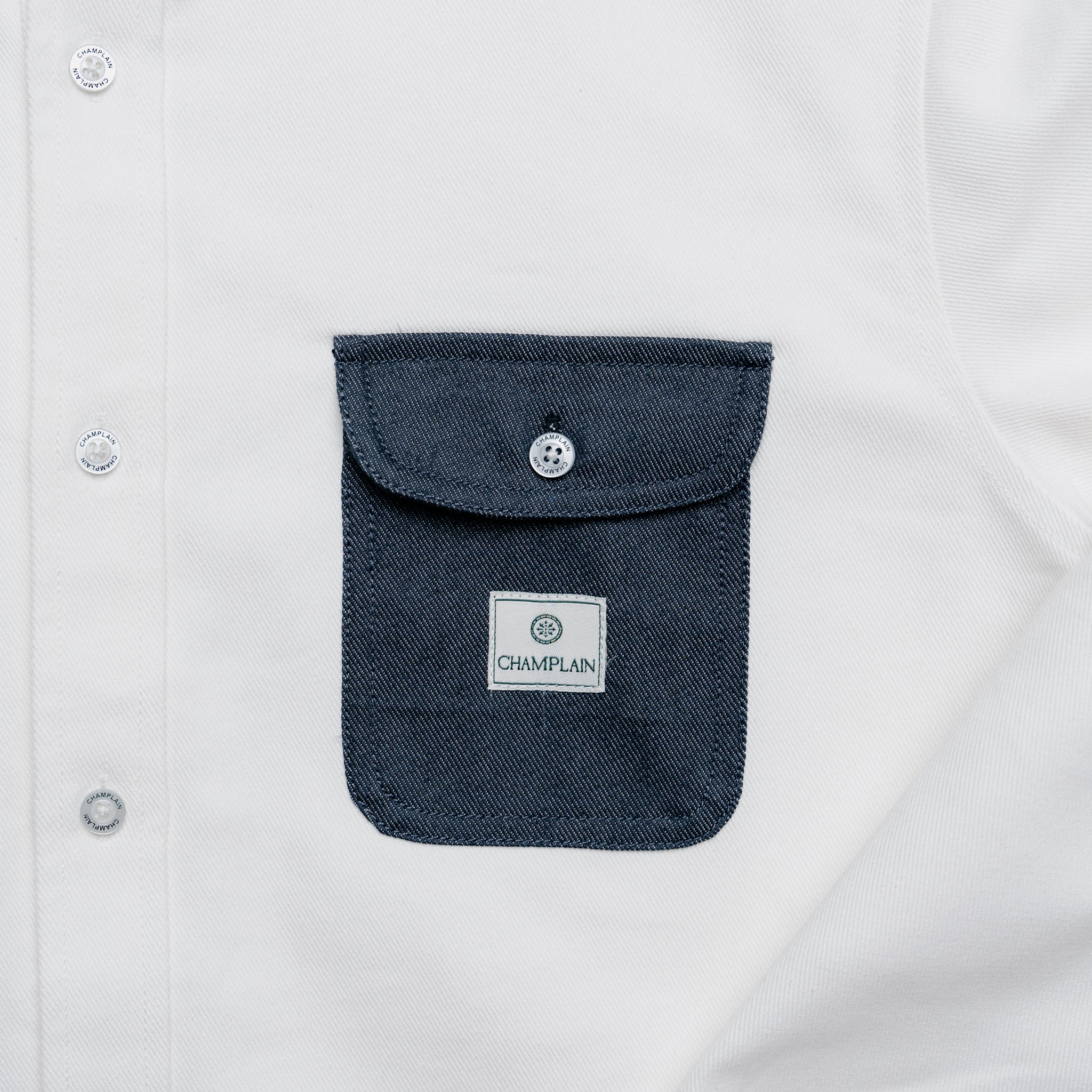 Close up of dark denim pocket on a white denim overshirt.