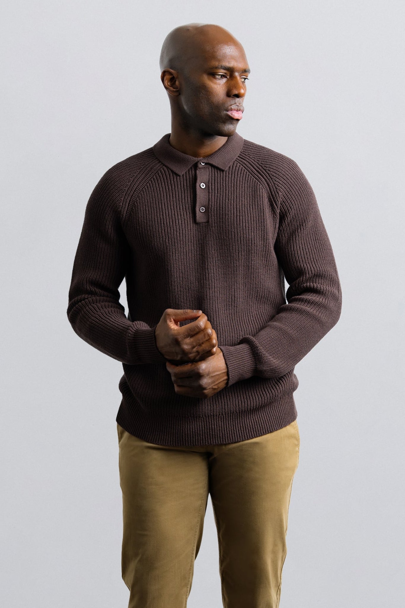 Man wearing a brown sweater and beige pants against a plain background