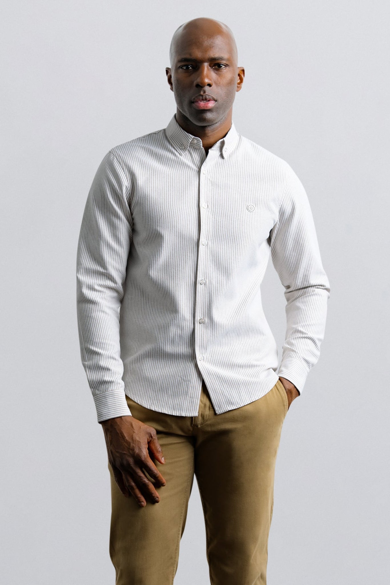 Man wearing a white button-up shirt and beige pants against a plain background