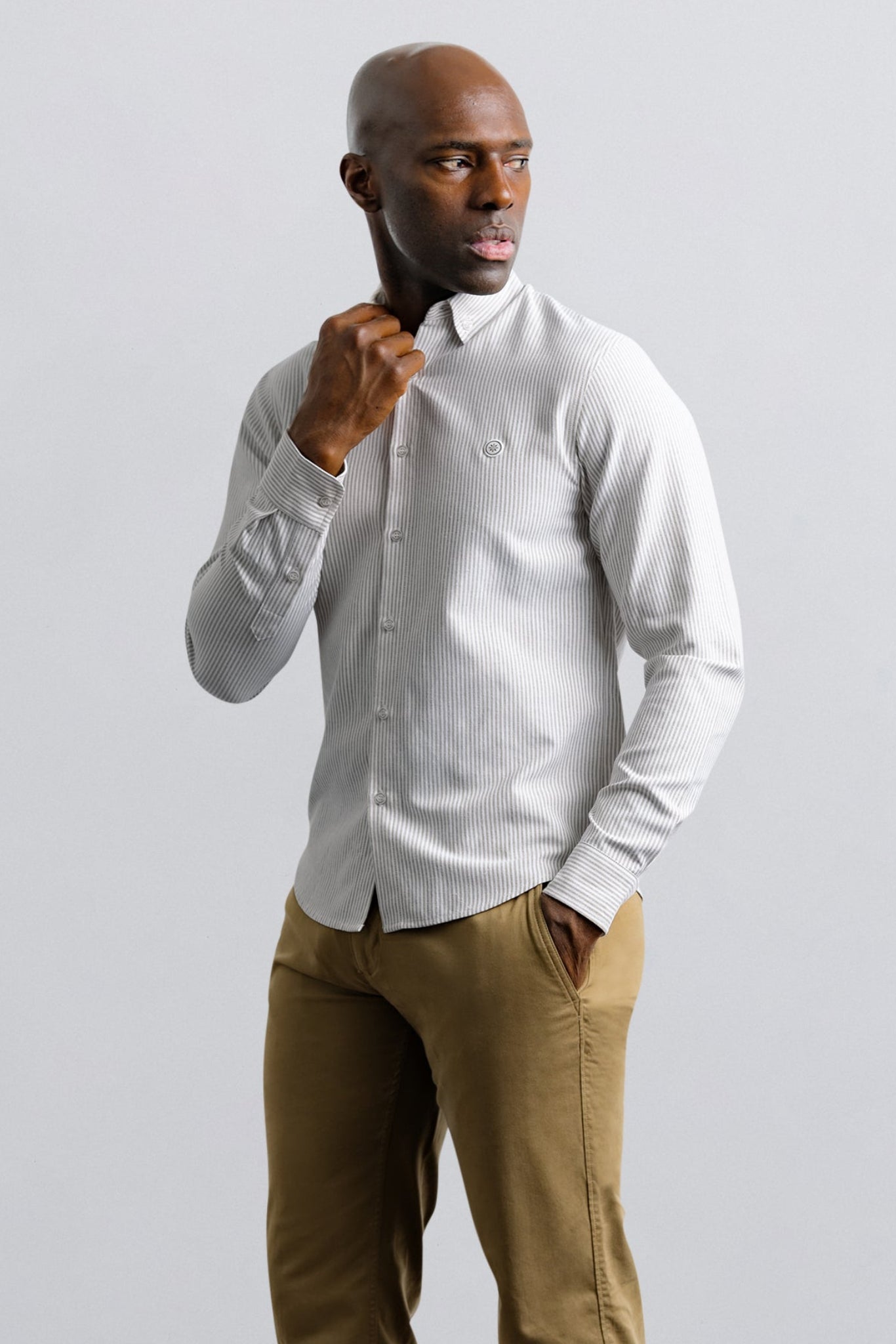 Man wearing a white shirt and brown pants against a light gray background