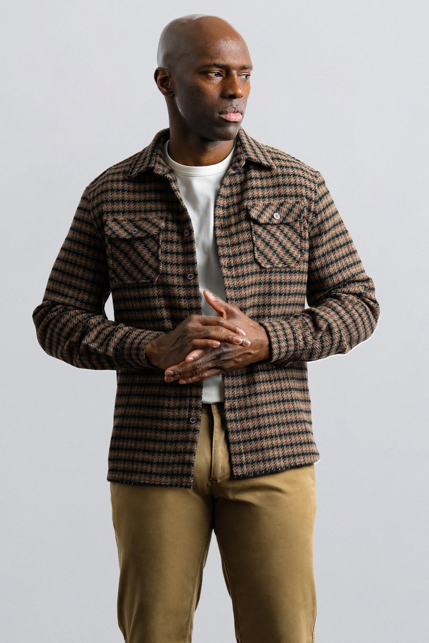 Man wearing a plaid shirt over a white t-shirt with beige pants on a light gray background