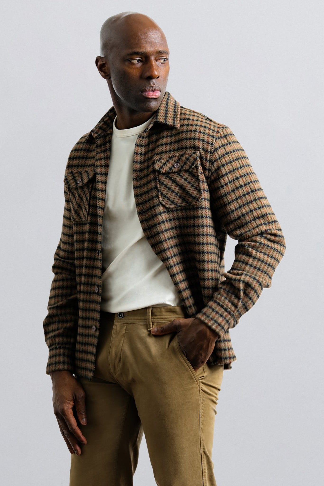 Man wearing a plaid shirt over a white t-shirt and khaki pants on a light gray background