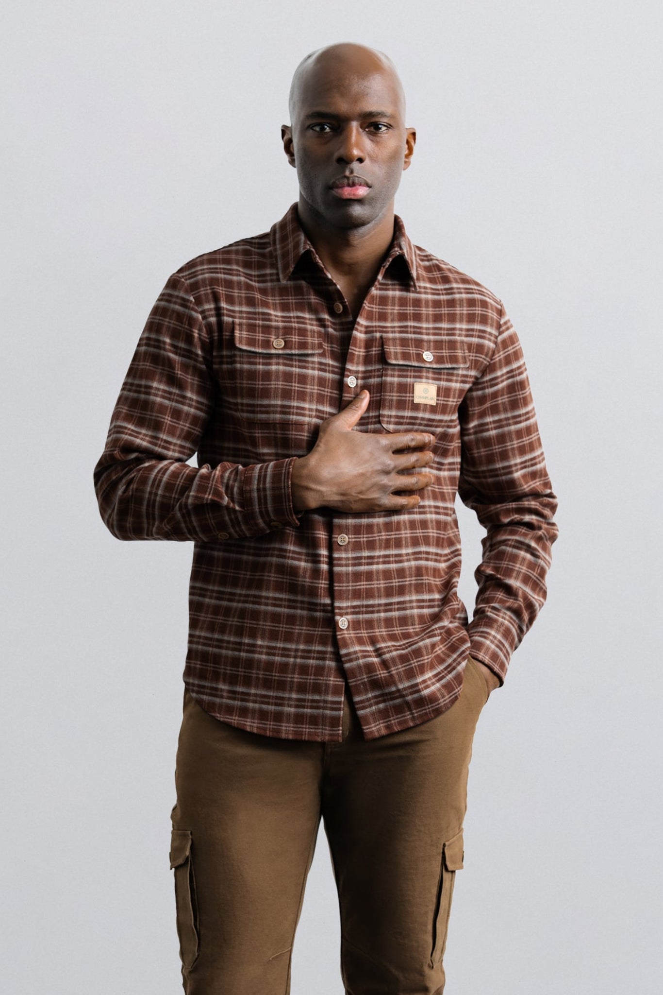Man wearing a plaid shirt and brown pants against a plain background
