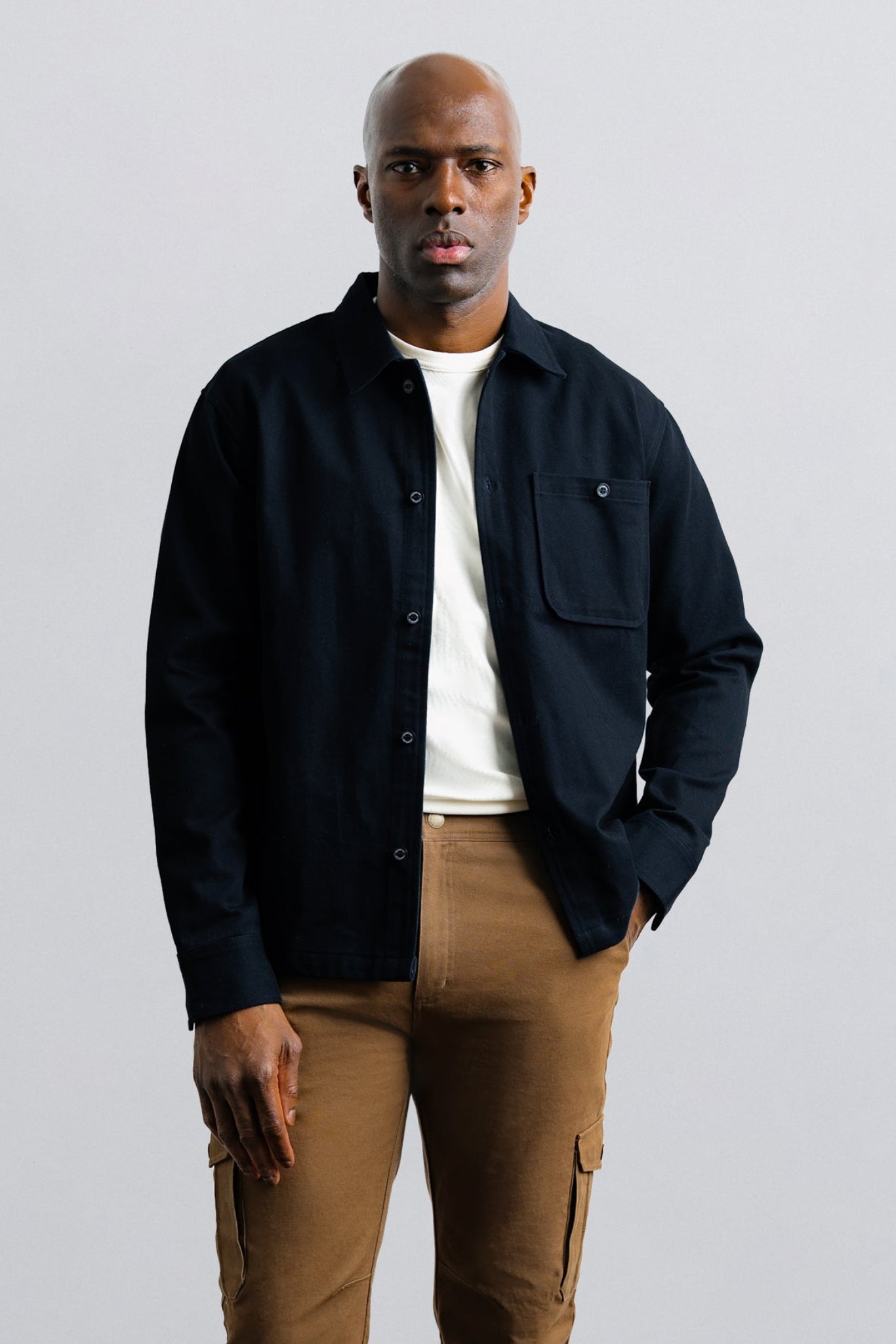 Man wearing a dark jacket and brown pants against a light gray background