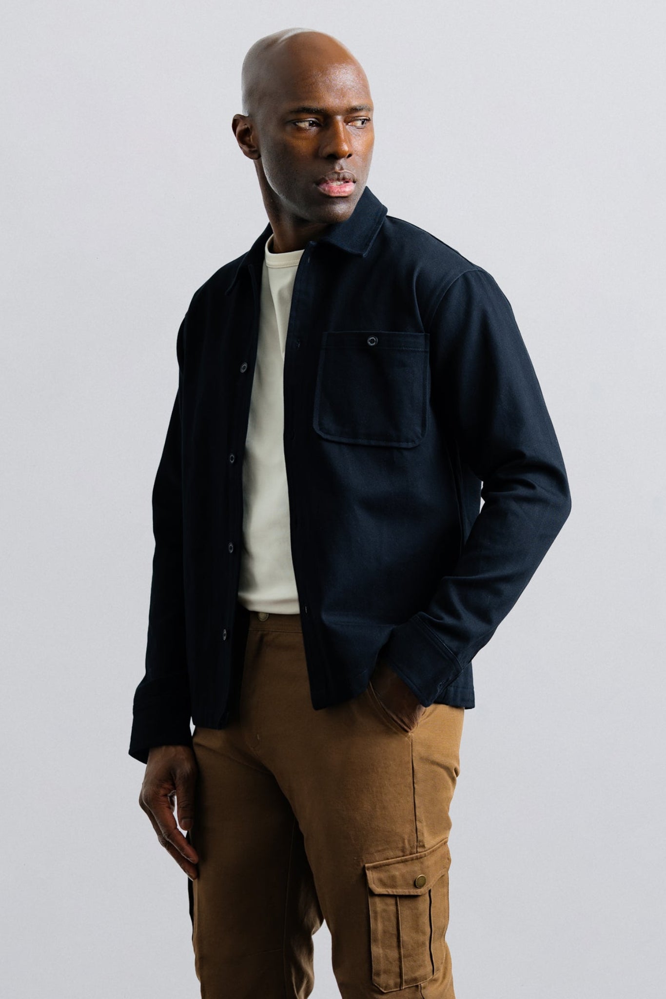 Man wearing a dark jacket and brown pants against a plain background