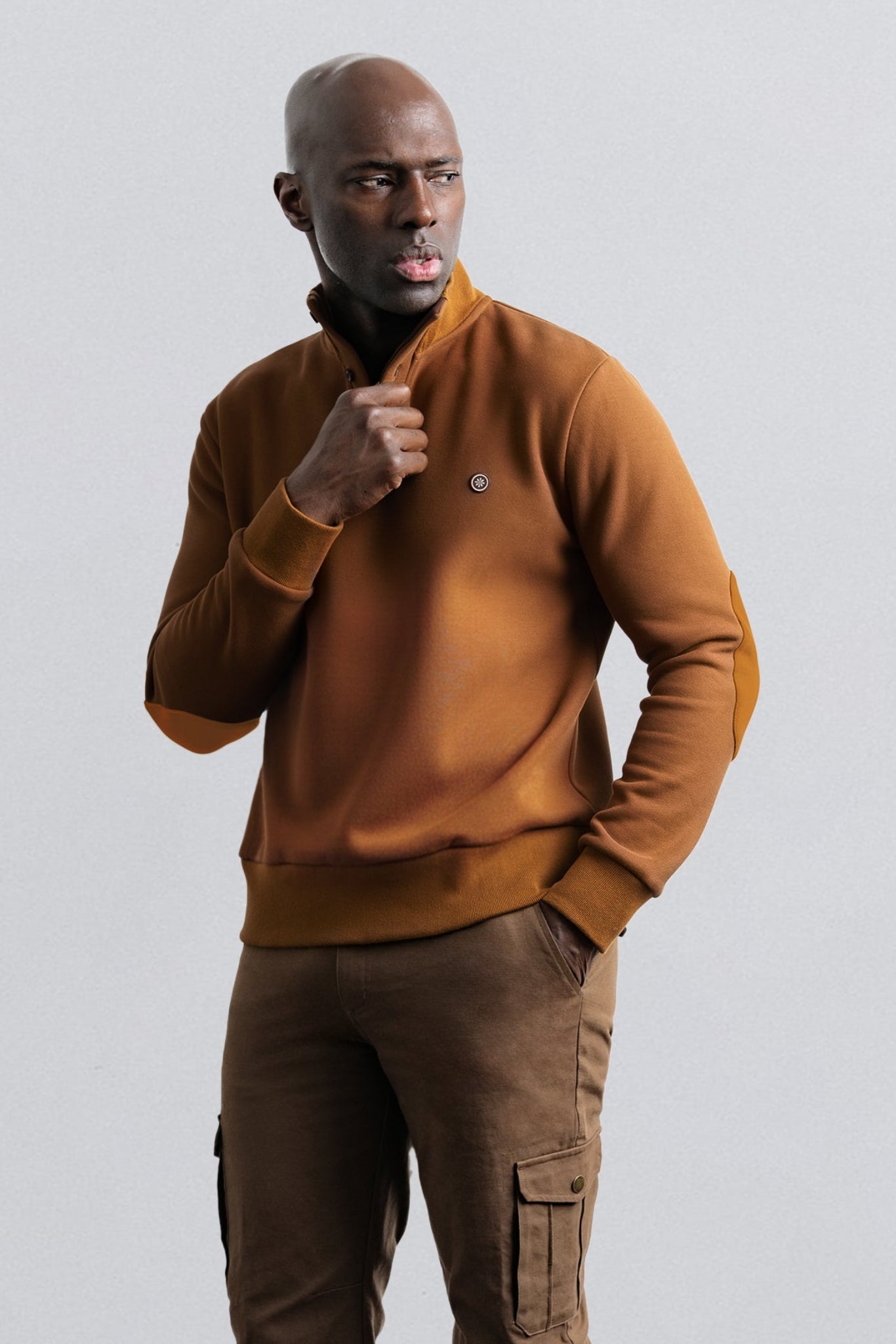 Man wearing a brown sweater and pants against a light gray background