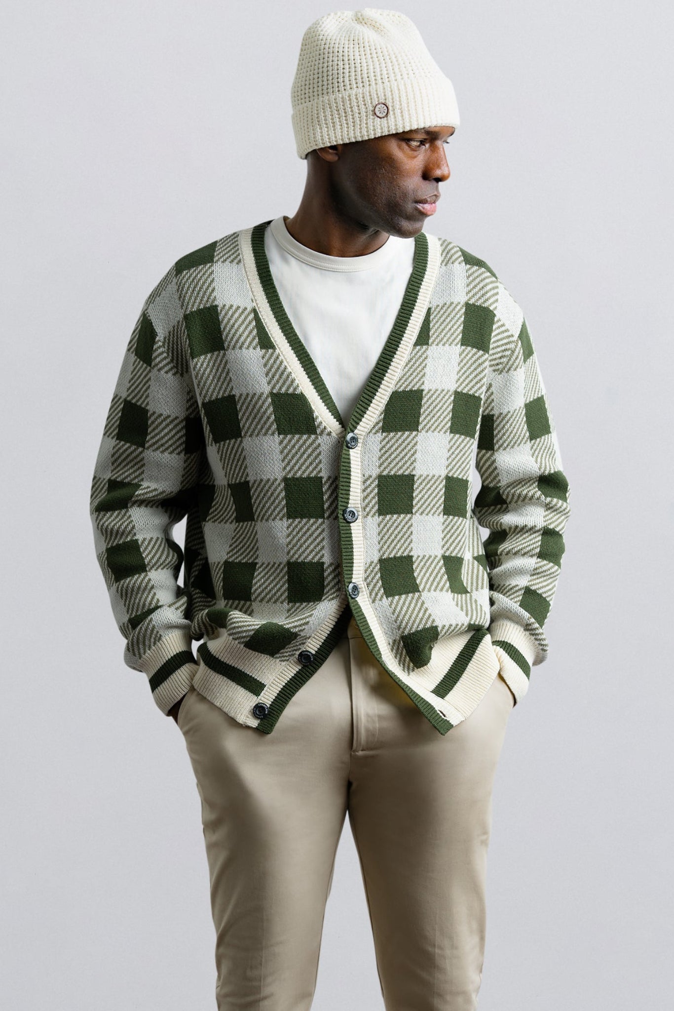 Person wearing a green and white checkered cardigan with beige pants and a white beanie on a light gray background