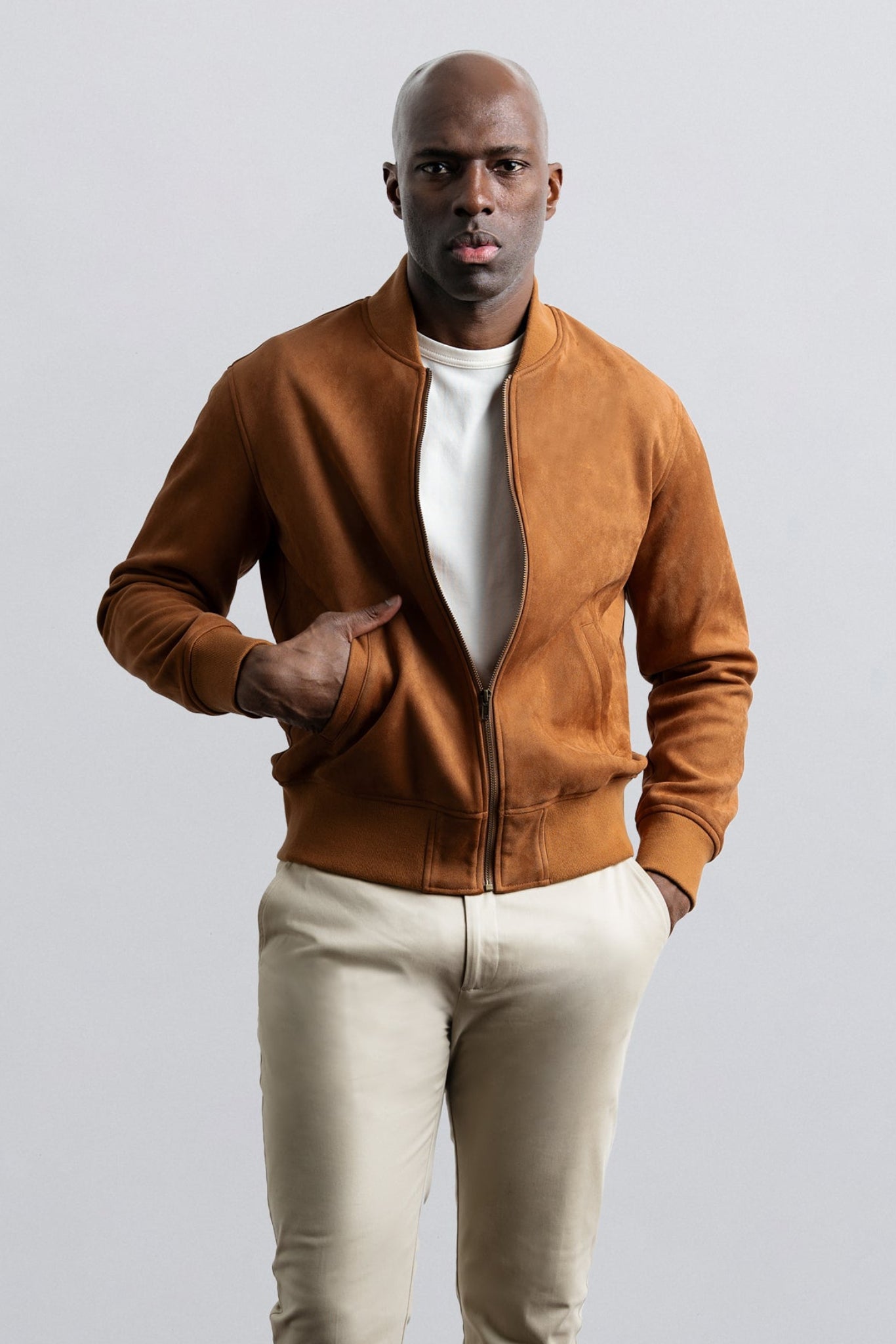 Man wearing a brown jacket and beige pants against a light gray background