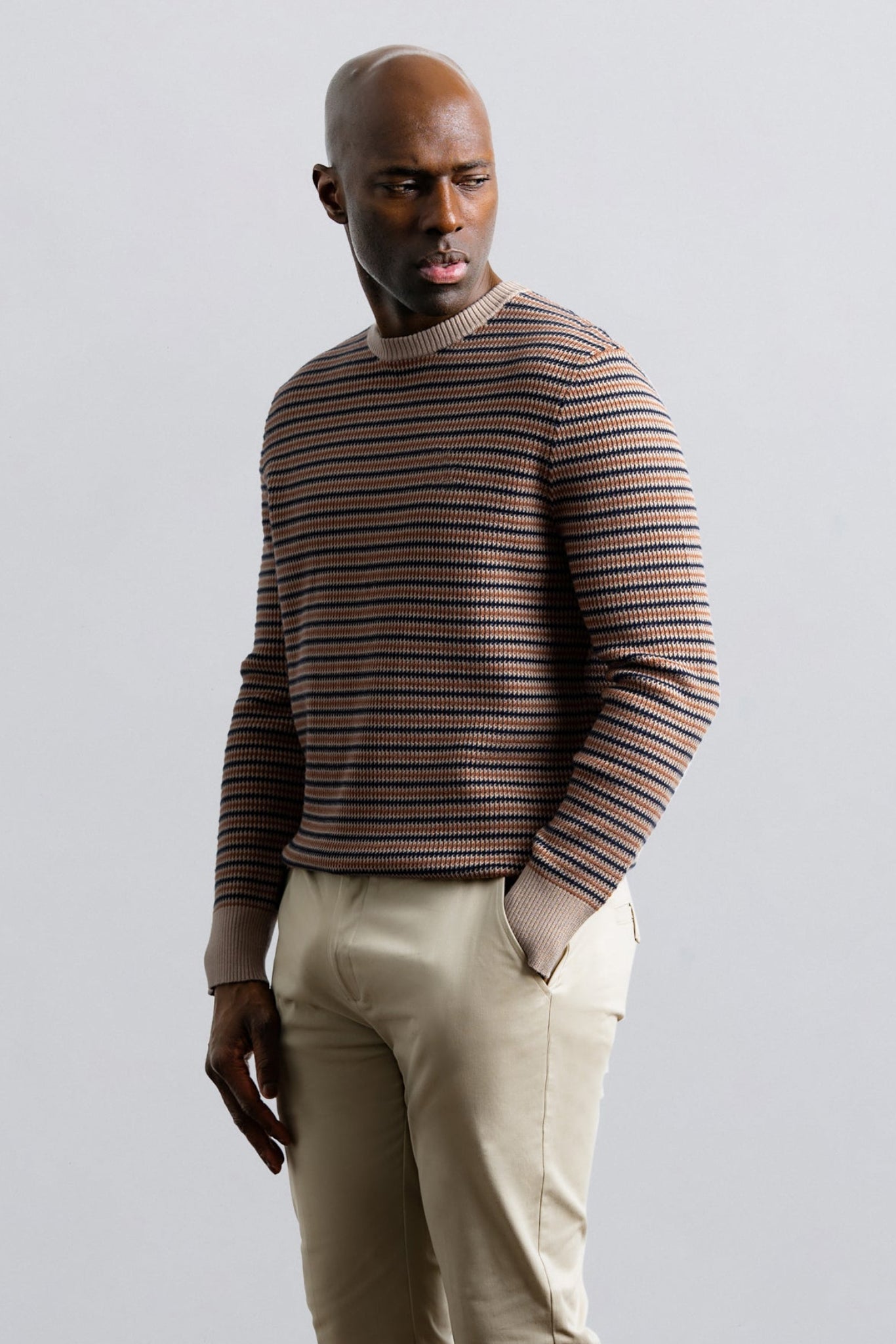 Man wearing a striped sweater and beige pants against a plain background