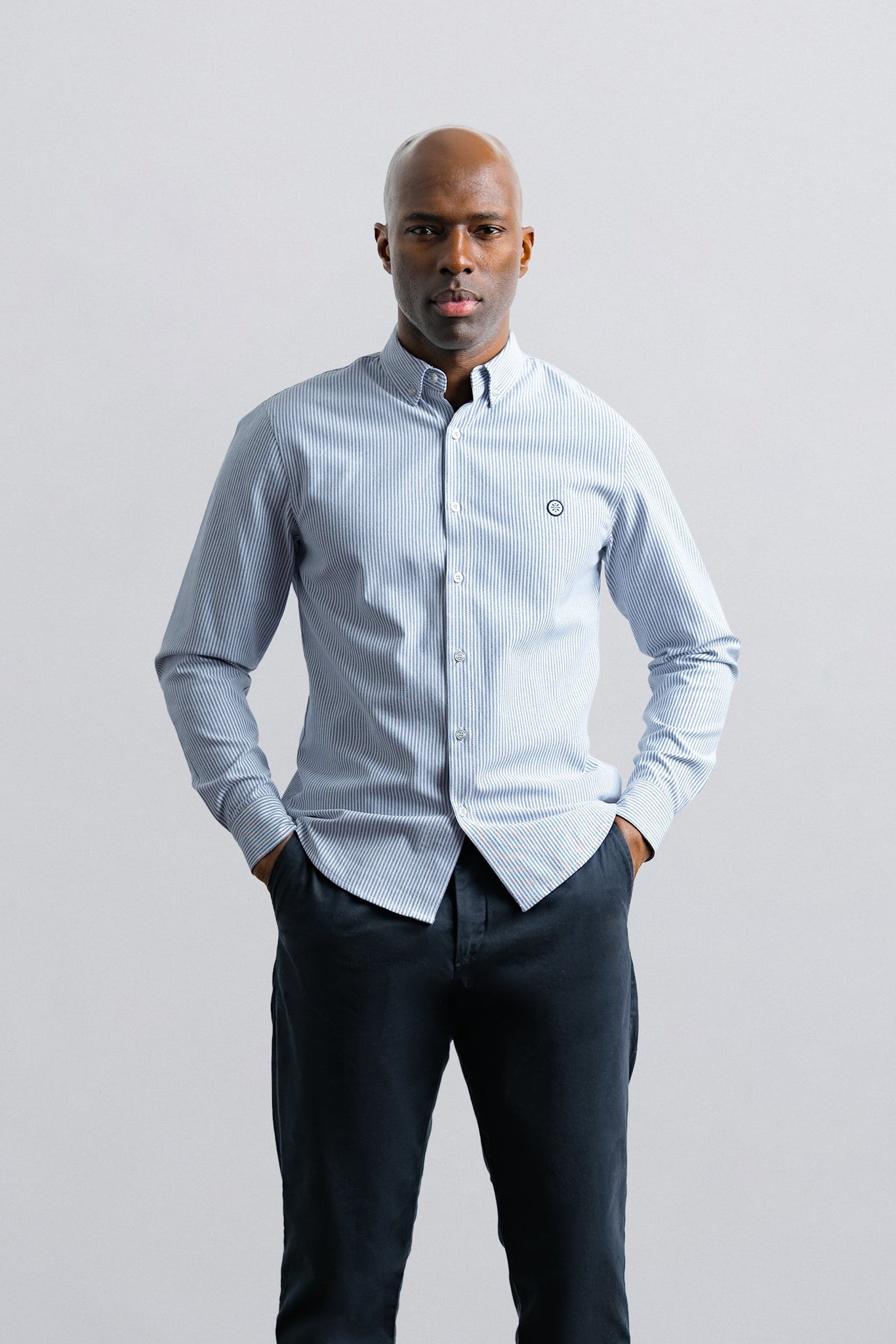 Man wearing a light blue button-up shirt and dark pants against a plain background