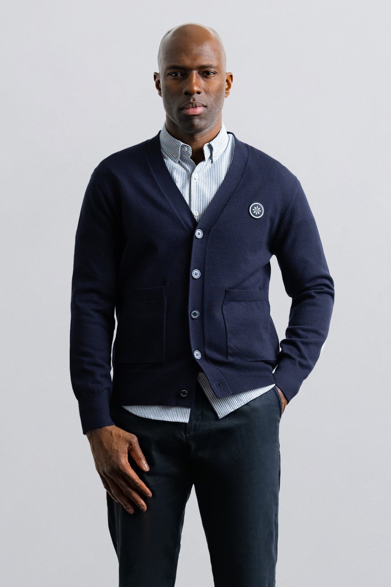 Man wearing a navy cardigan over a white shirt with a logo on a light gray background
