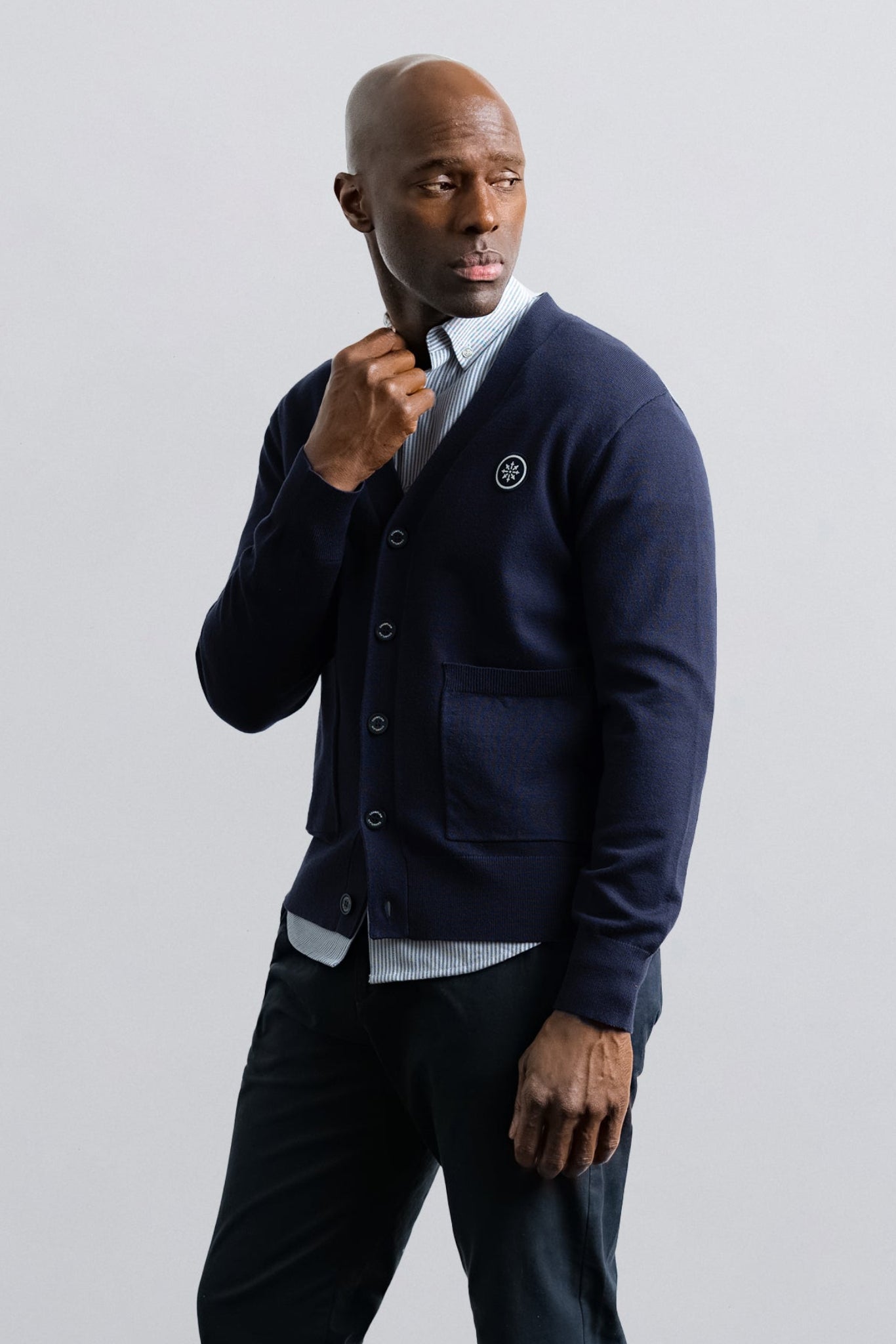 Man wearing a navy cardigan over a light shirt with dark pants on a plain background