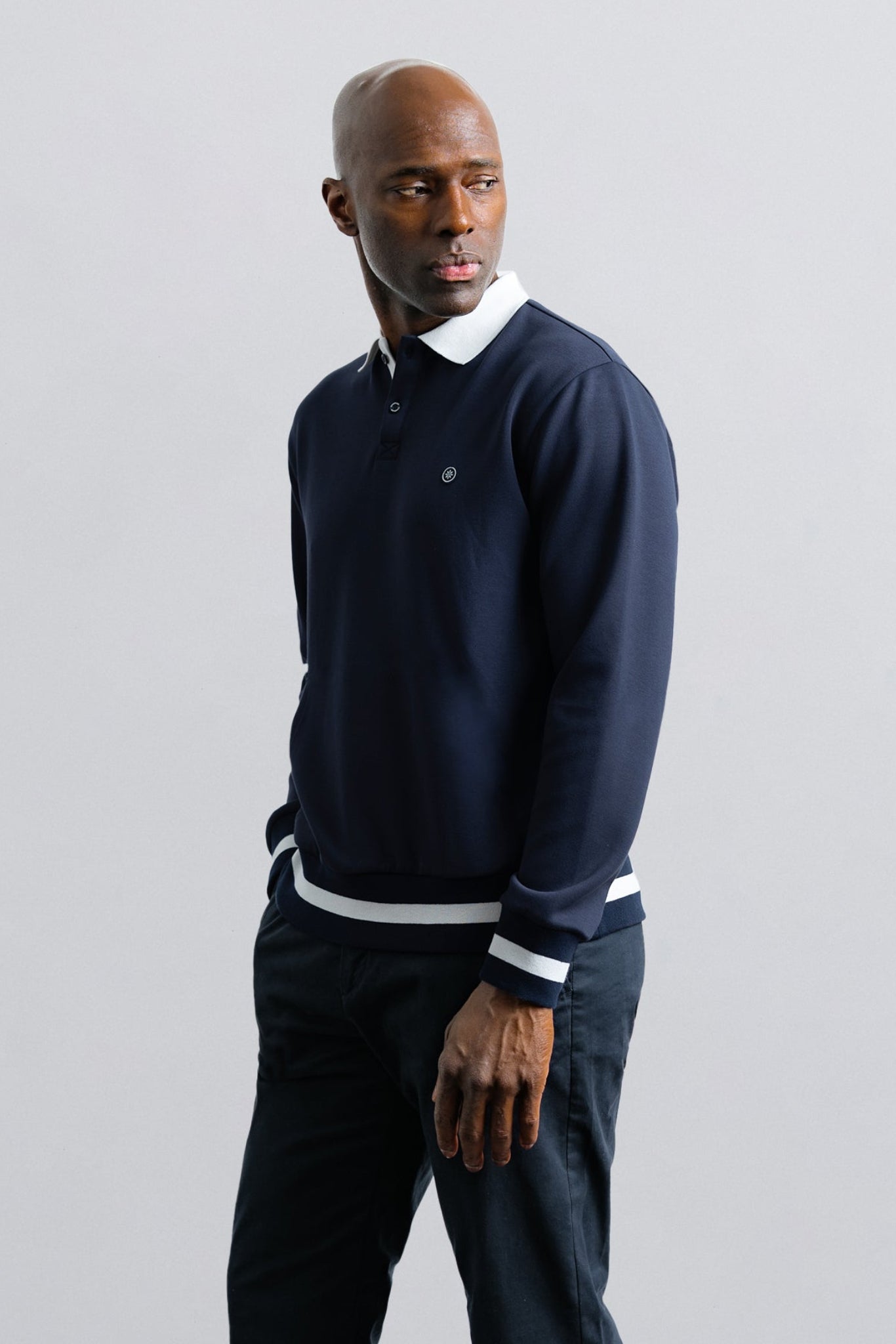 Man wearing a navy sweater with white collar and cuffs against a light gray background