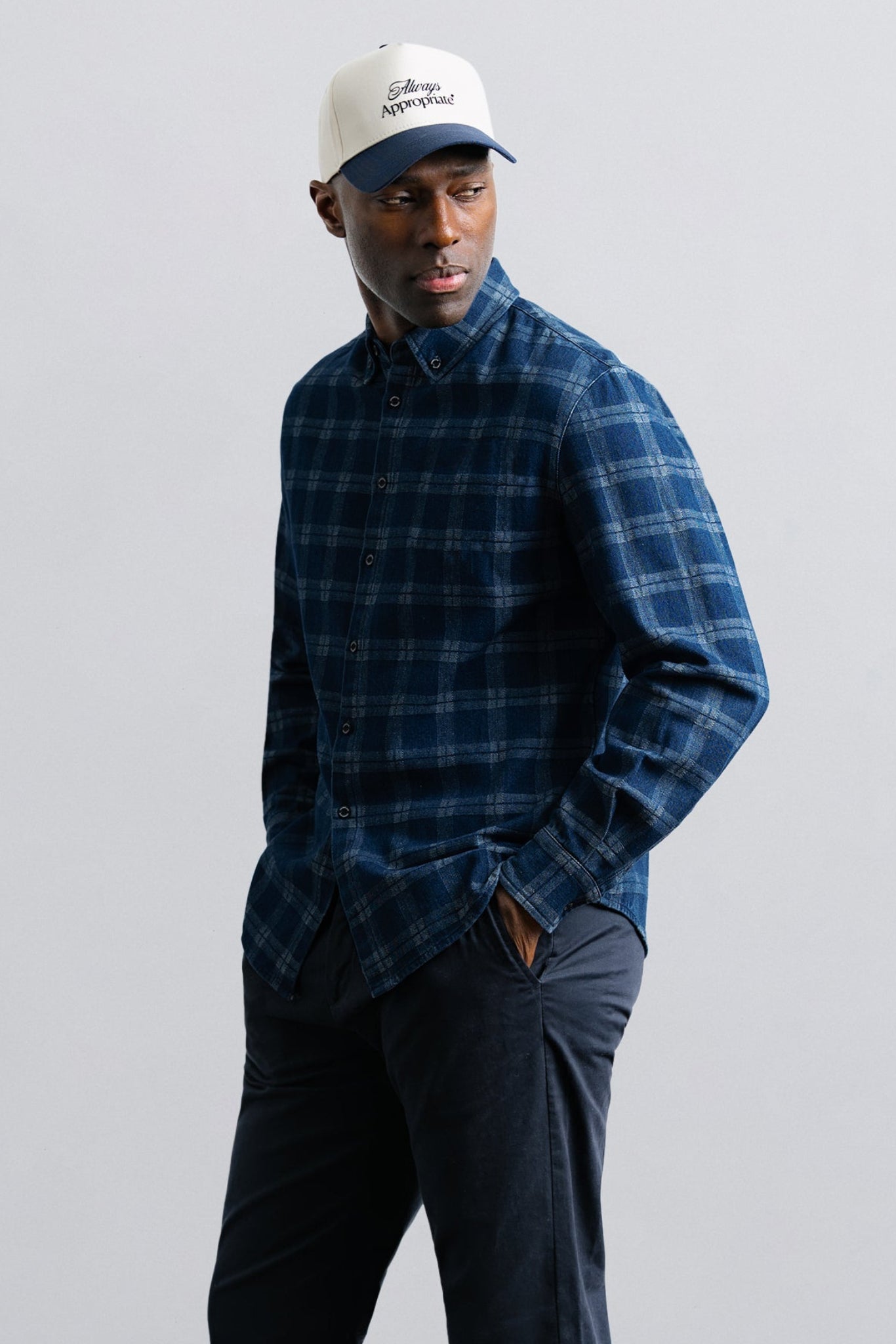 Man wearing a blue plaid shirt and cap against a light gray background