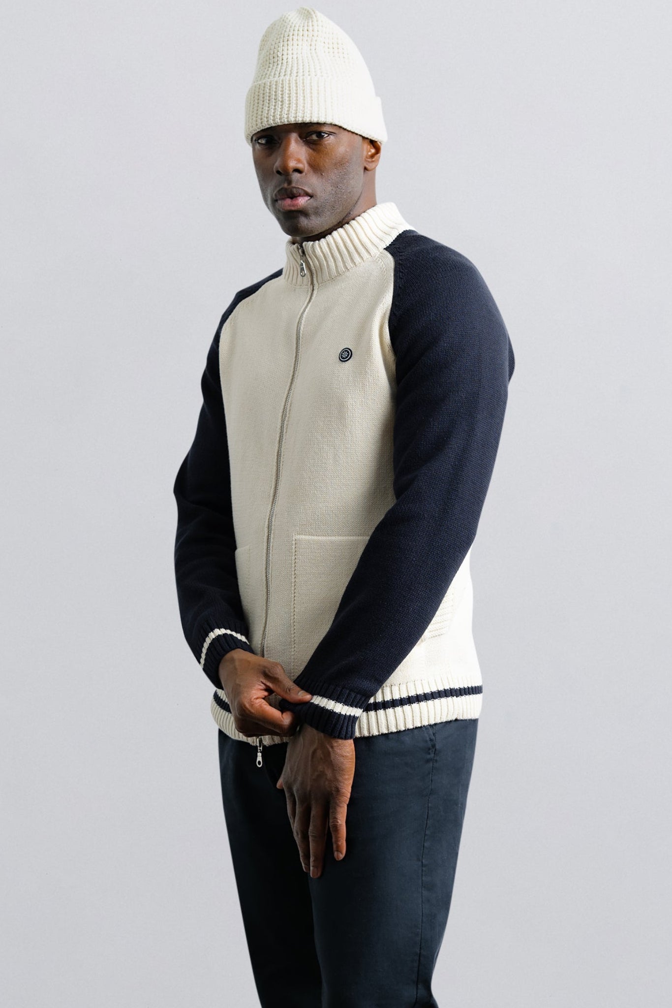 Person wearing a two-tone sweater and white beanie on a plain background