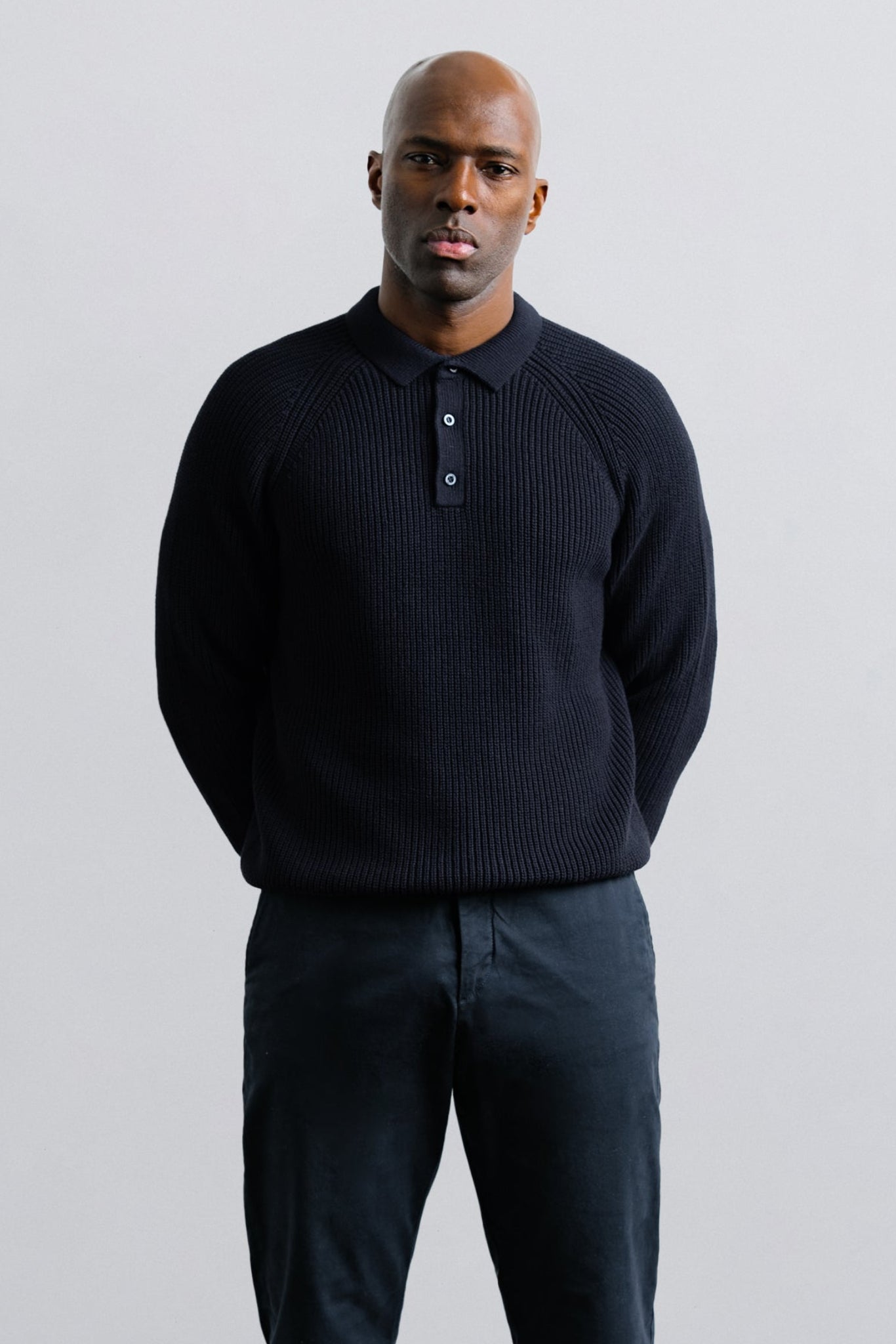Man wearing a dark sweater and pants against a light gray background