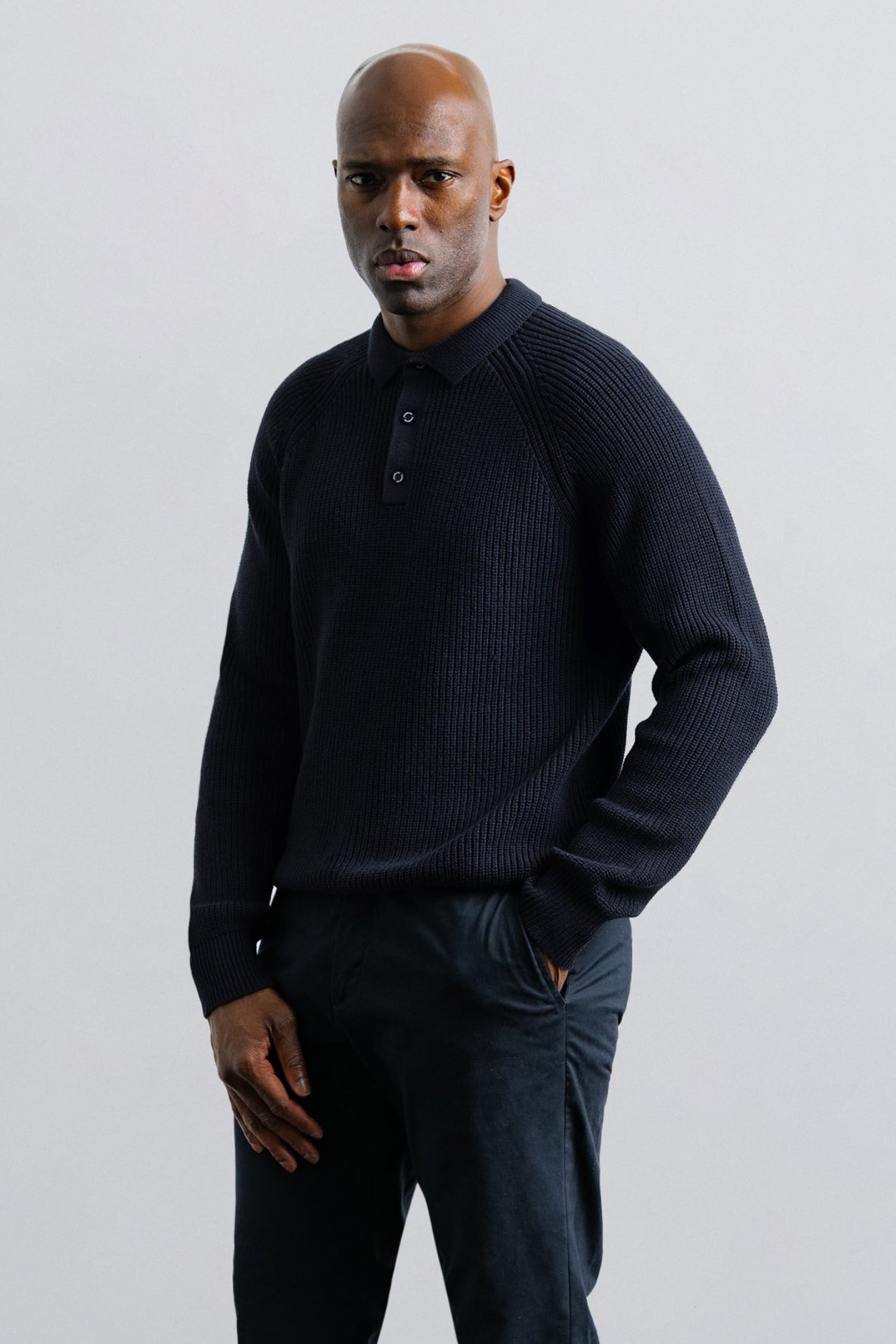 Man wearing a dark blue sweater and pants against a light gray background