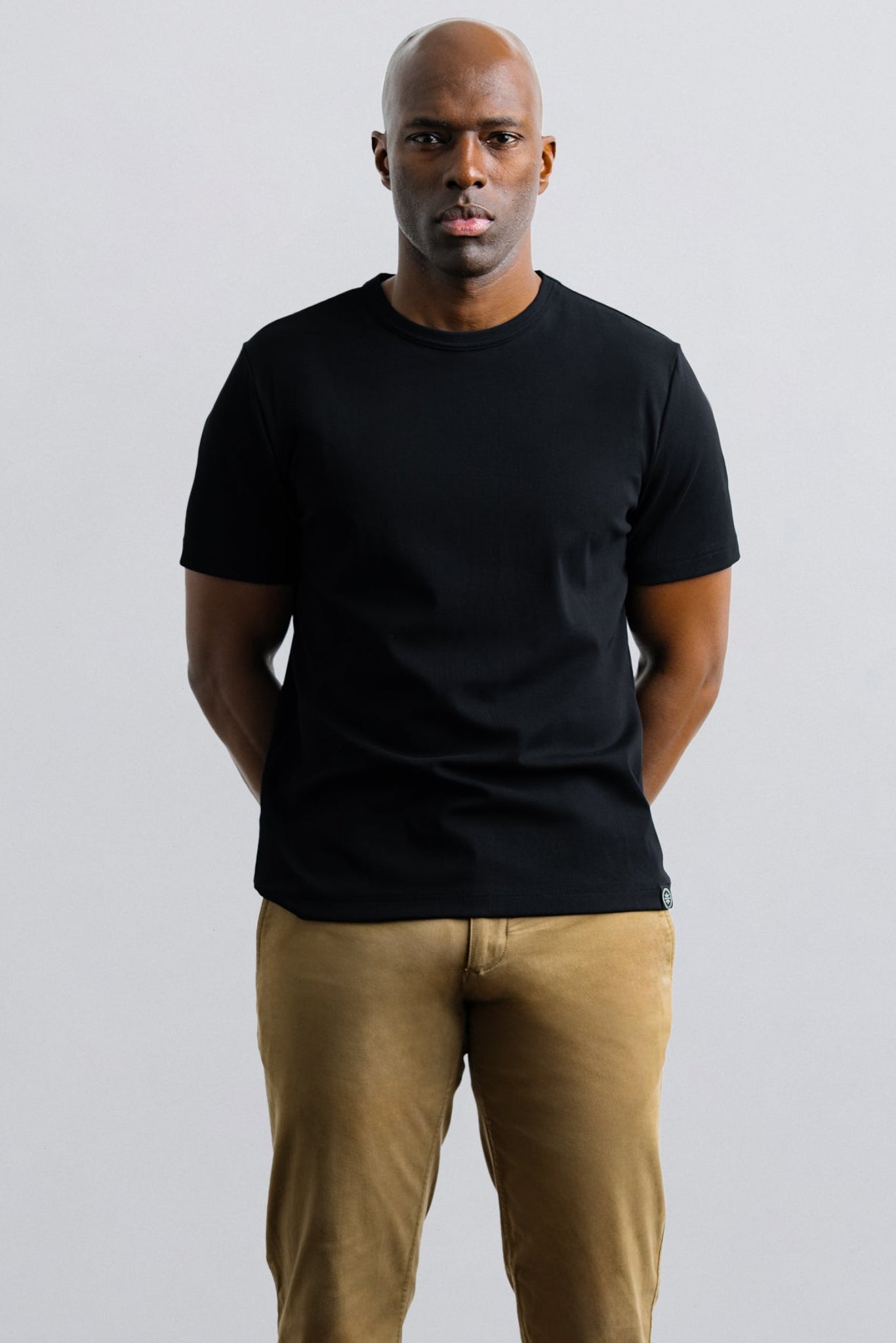 Man wearing a black t-shirt and beige pants against a plain background
