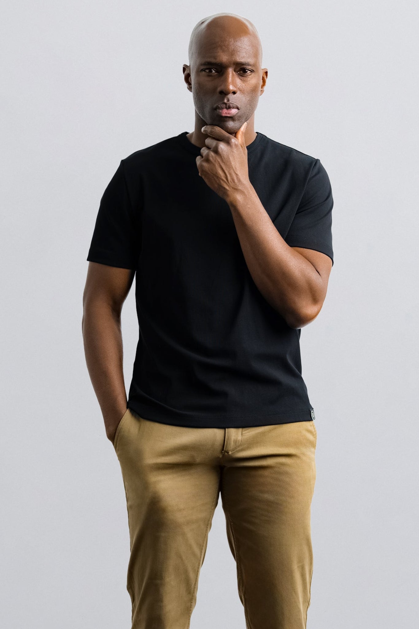 Man wearing a black t-shirt and beige pants against a light gray background