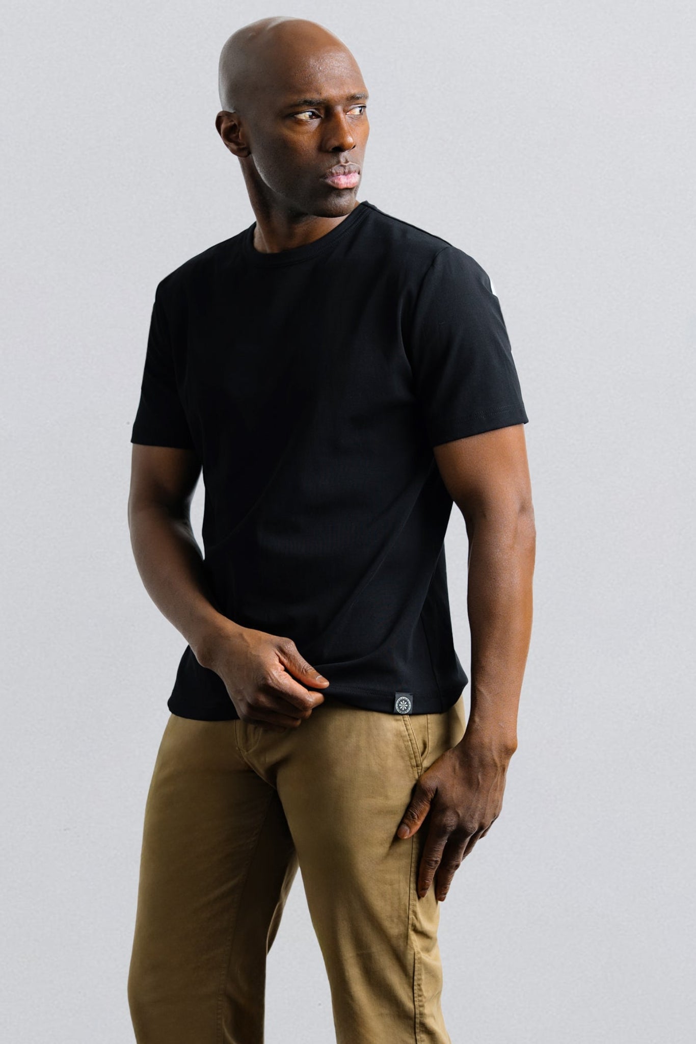 Man wearing a black t-shirt and brown pants against a light gray background