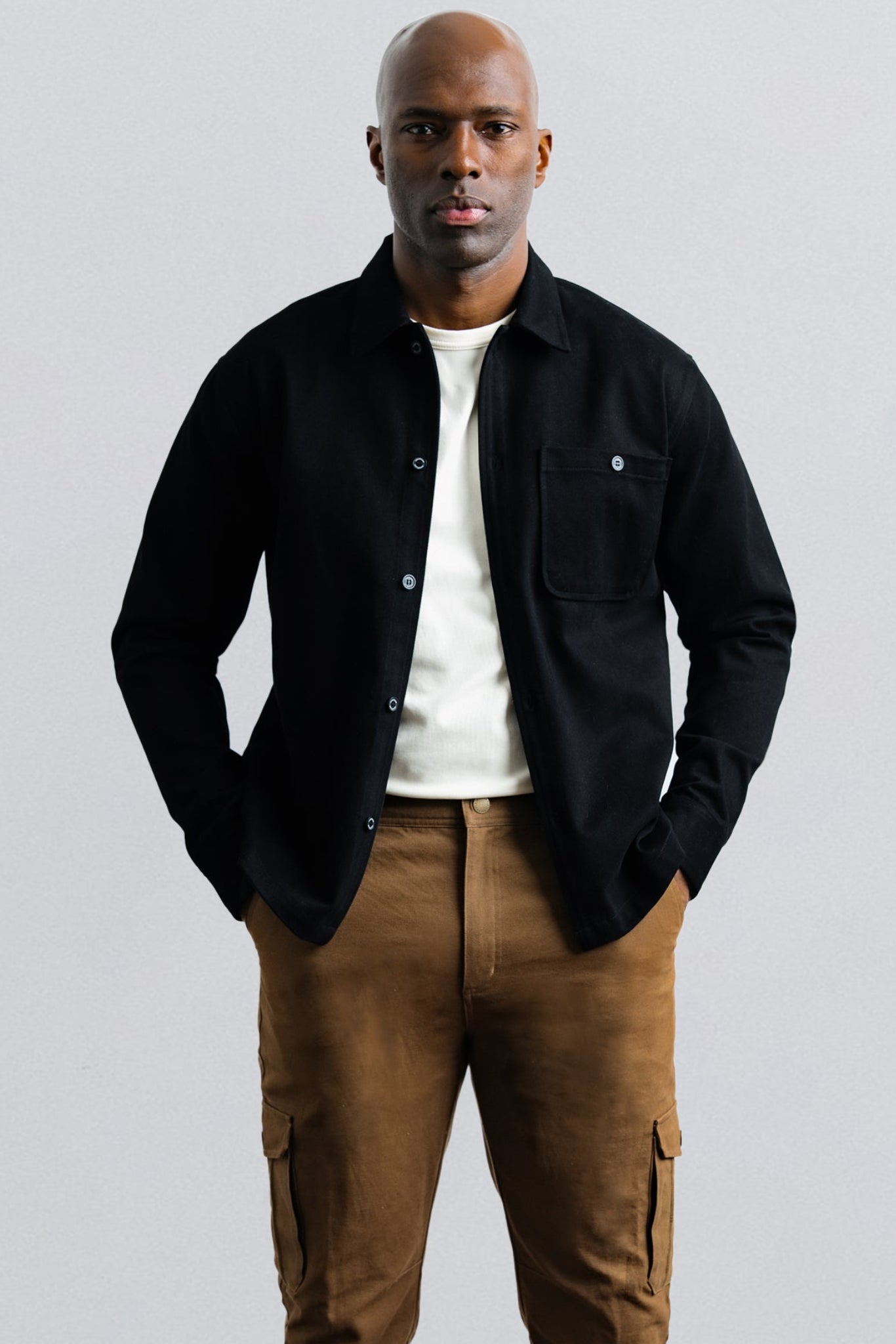 Man wearing a black jacket and brown pants against a light gray background