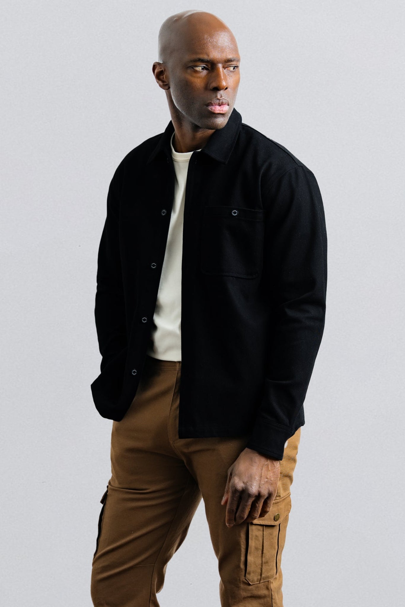 Man wearing a black jacket and brown pants on a light gray background