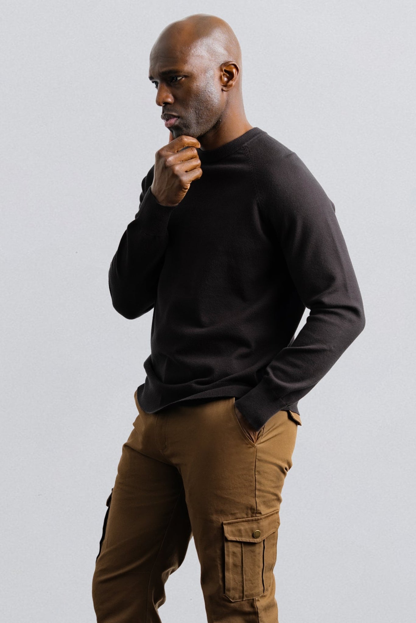 Man wearing a black sweater and brown cargo pants on a light gray background