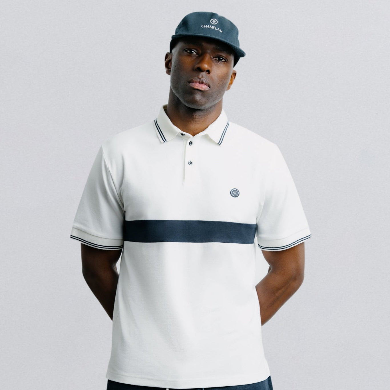 Man wearing a white polo shirt with a navy stripe and navy shorts on a light gray background