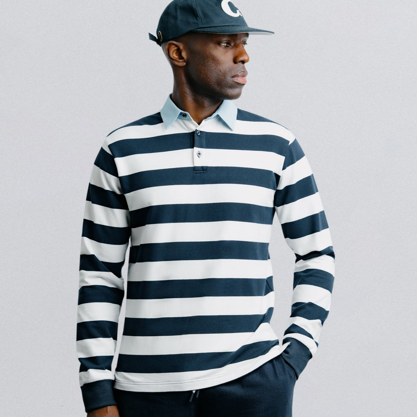 Man wearing a navy and white striped shirt with a cap on a gray background