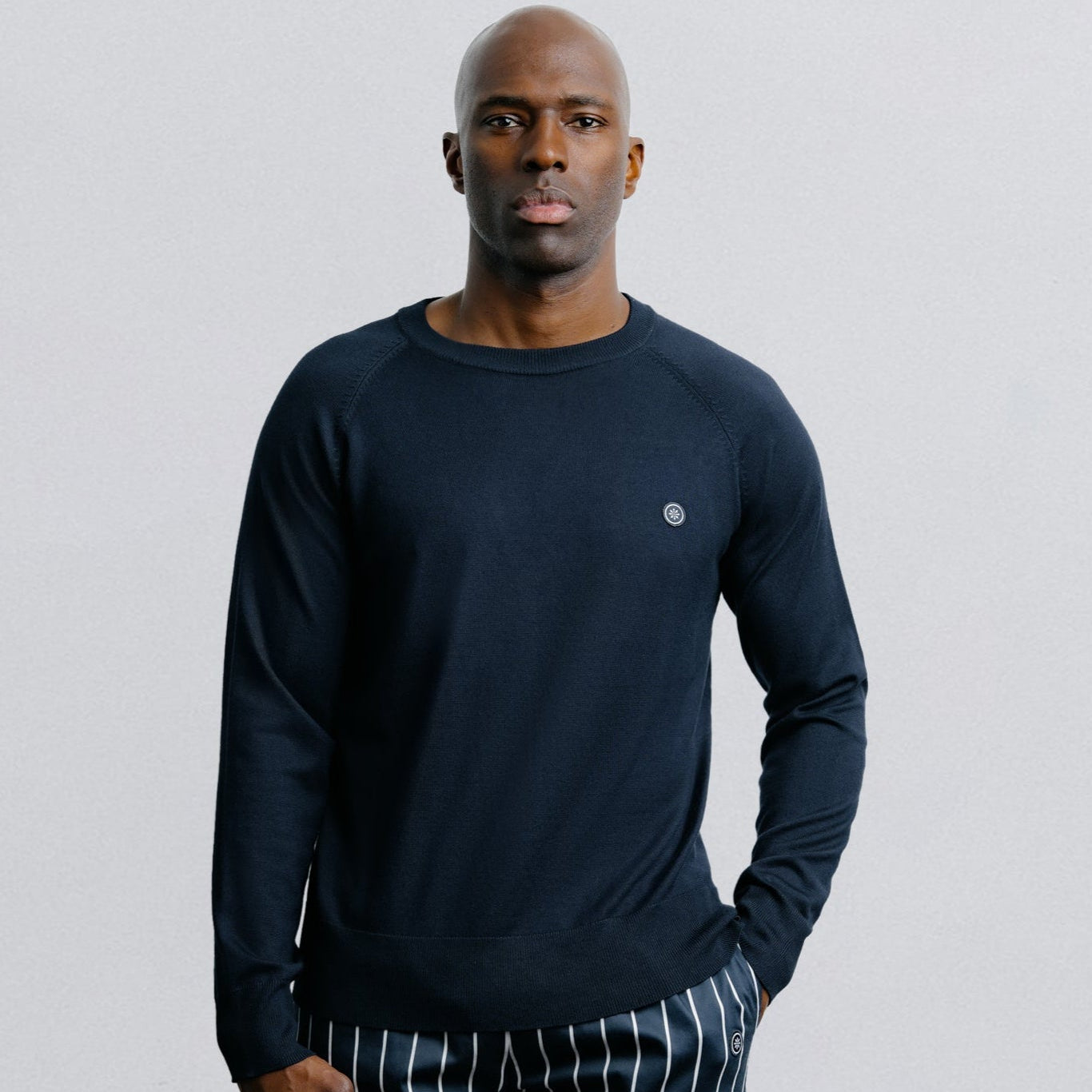 Man wearing a navy long-sleeve shirt and striped shorts on a light gray background