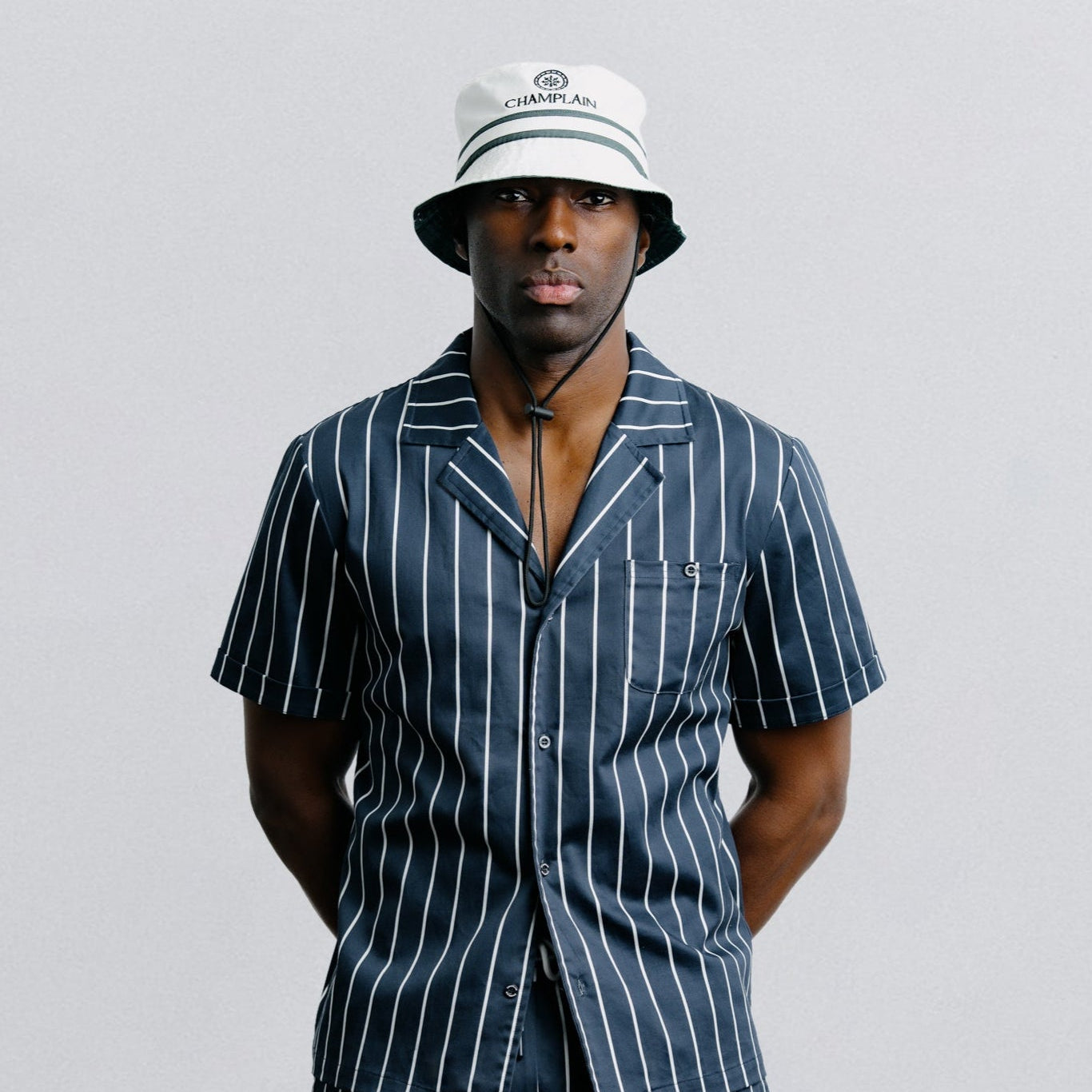 Man wearing a navy pinstripe outfit with a white hat on a light gray background