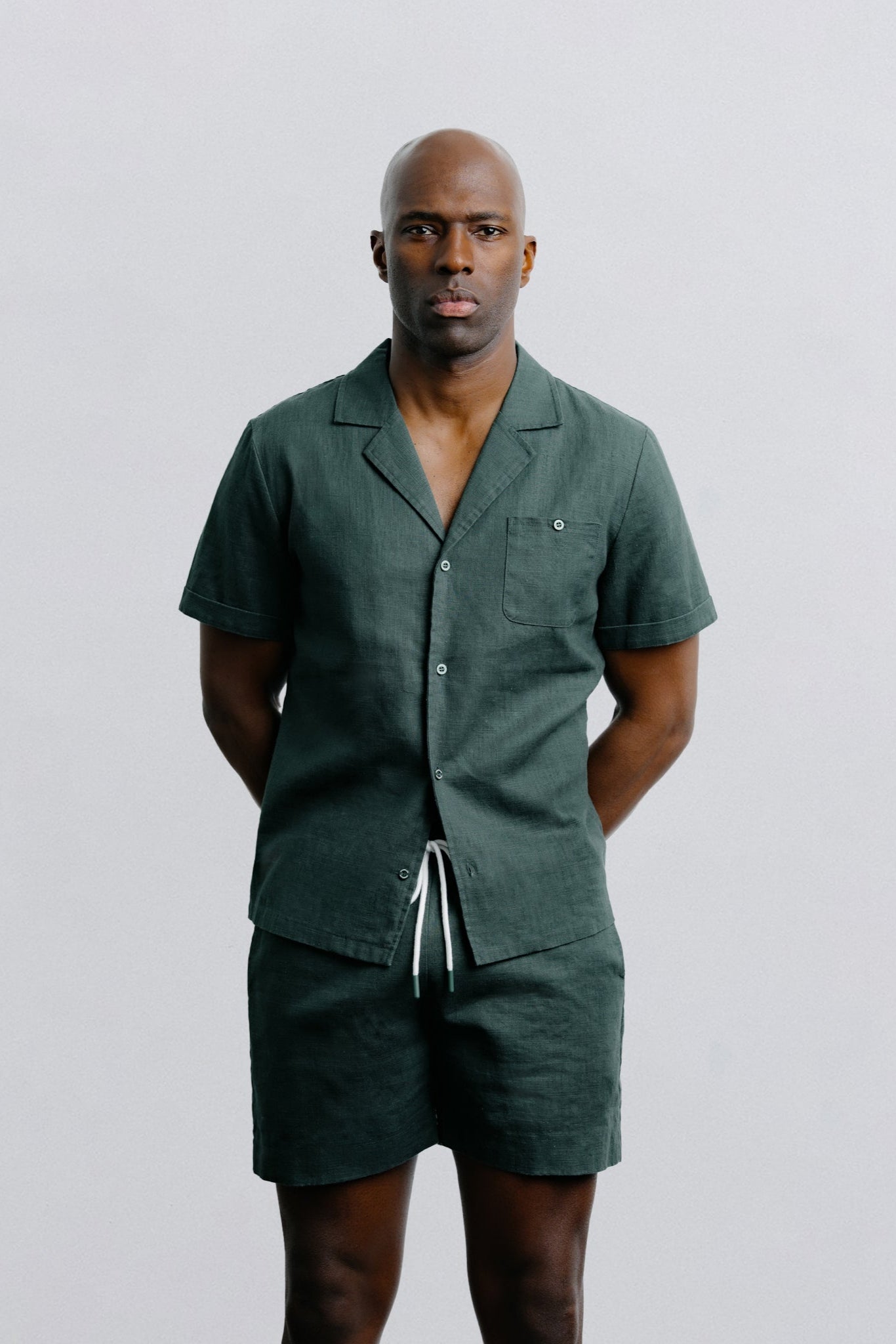 Man wearing a green shirt and shorts set against a plain background