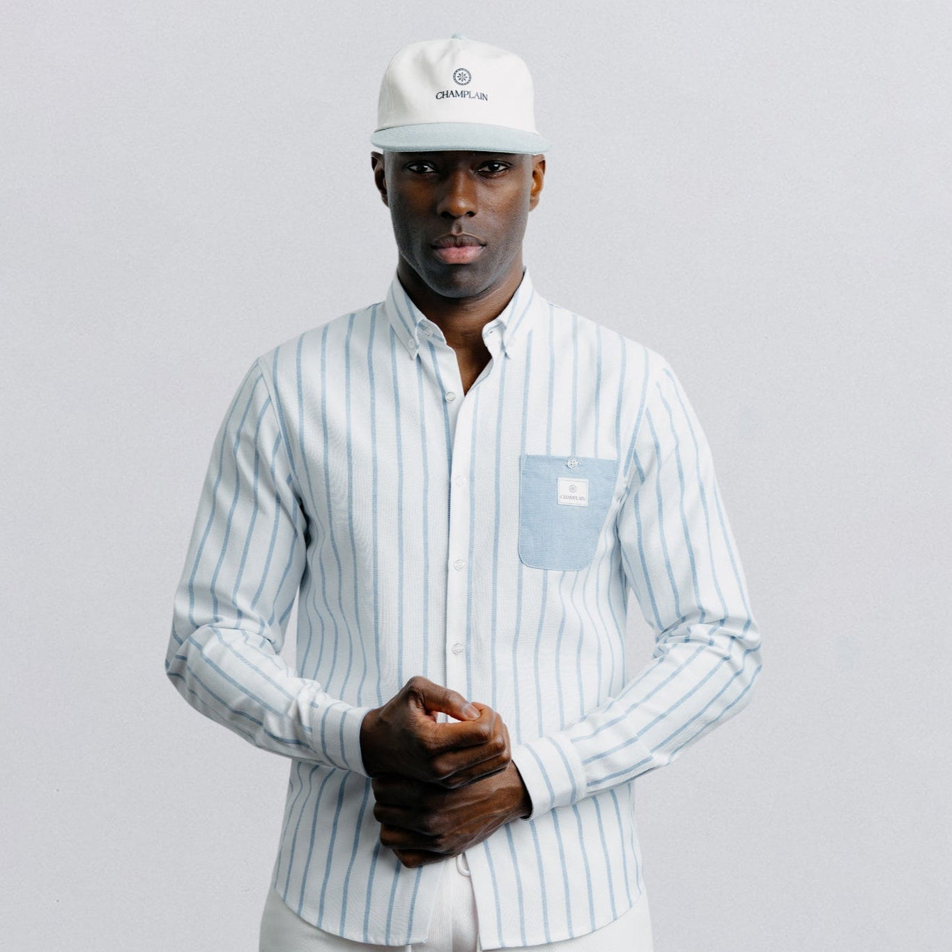 Man wearing a striped shirt and shorts with a white cap on a light gray background